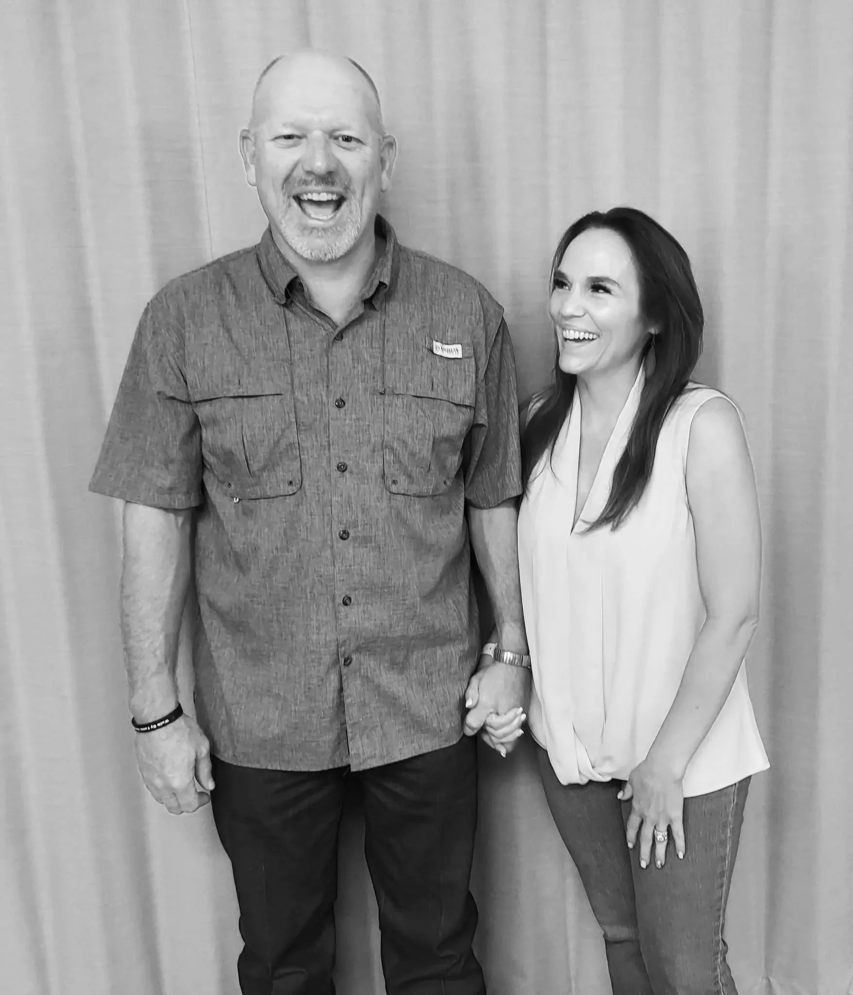A man and woman holding hands and smiling, standing in front of a curtain.