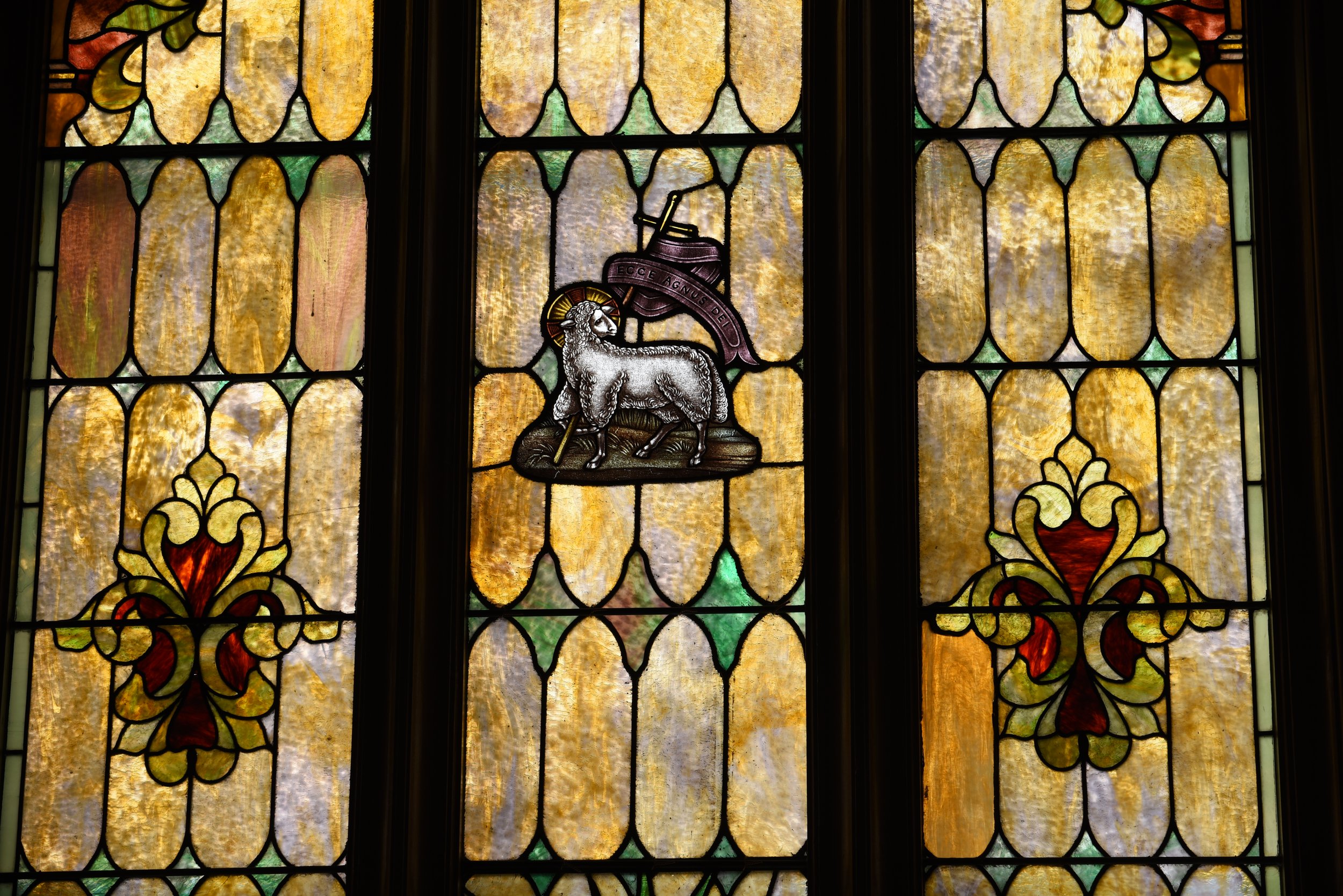 Stained glass window featuring a coat of arms with a lion and a ribbon banner with Latin text.