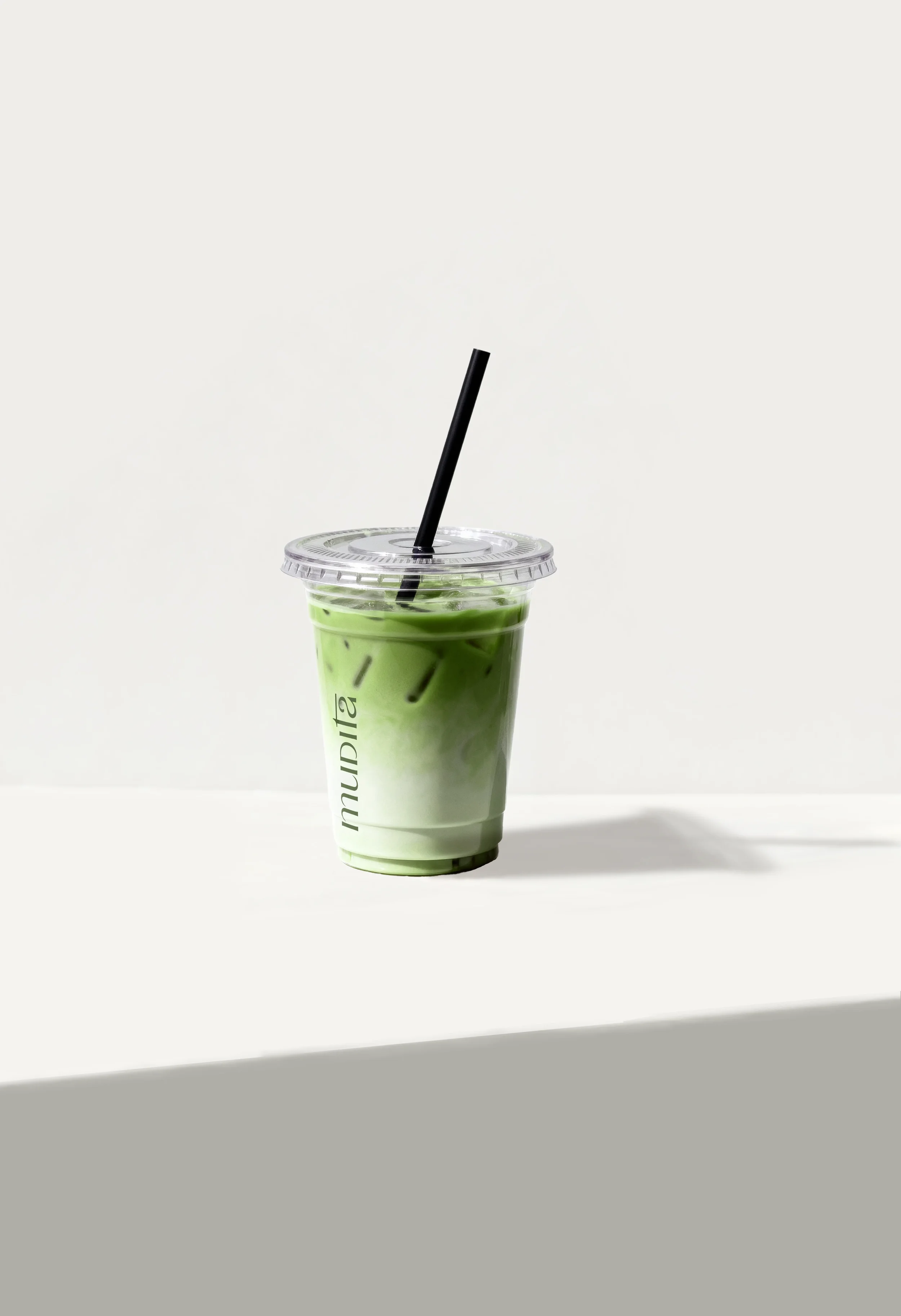 Vaso plástico con bebida verde, con tapa y popote negro, en fondo blanco