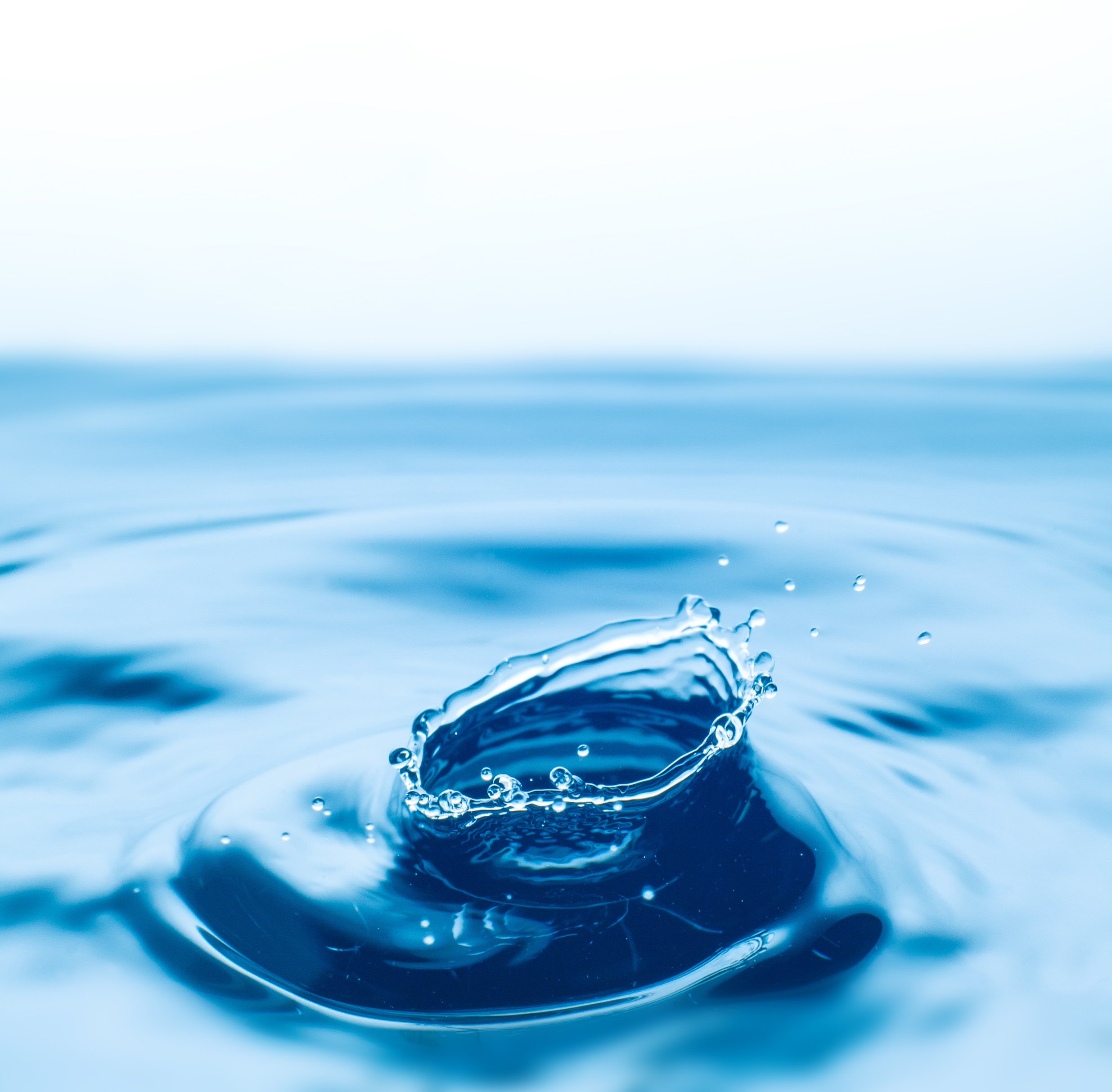 Close-up of a water droplet hitting the surface of a calm body of water, creating a splash and ripples.