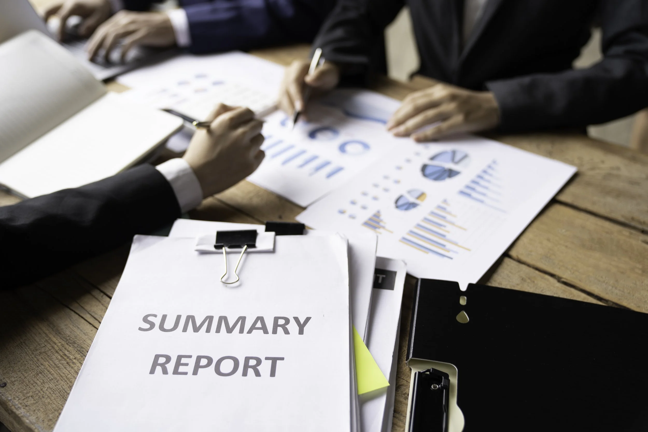 People working on a business presentation with charts and graphs at a wooden table, with a summarized report and documents.