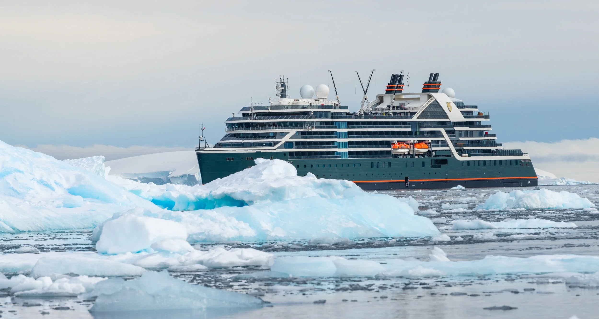 A large cruise ship navigating through icy waters with floating icebergs and snow-covered landscape.