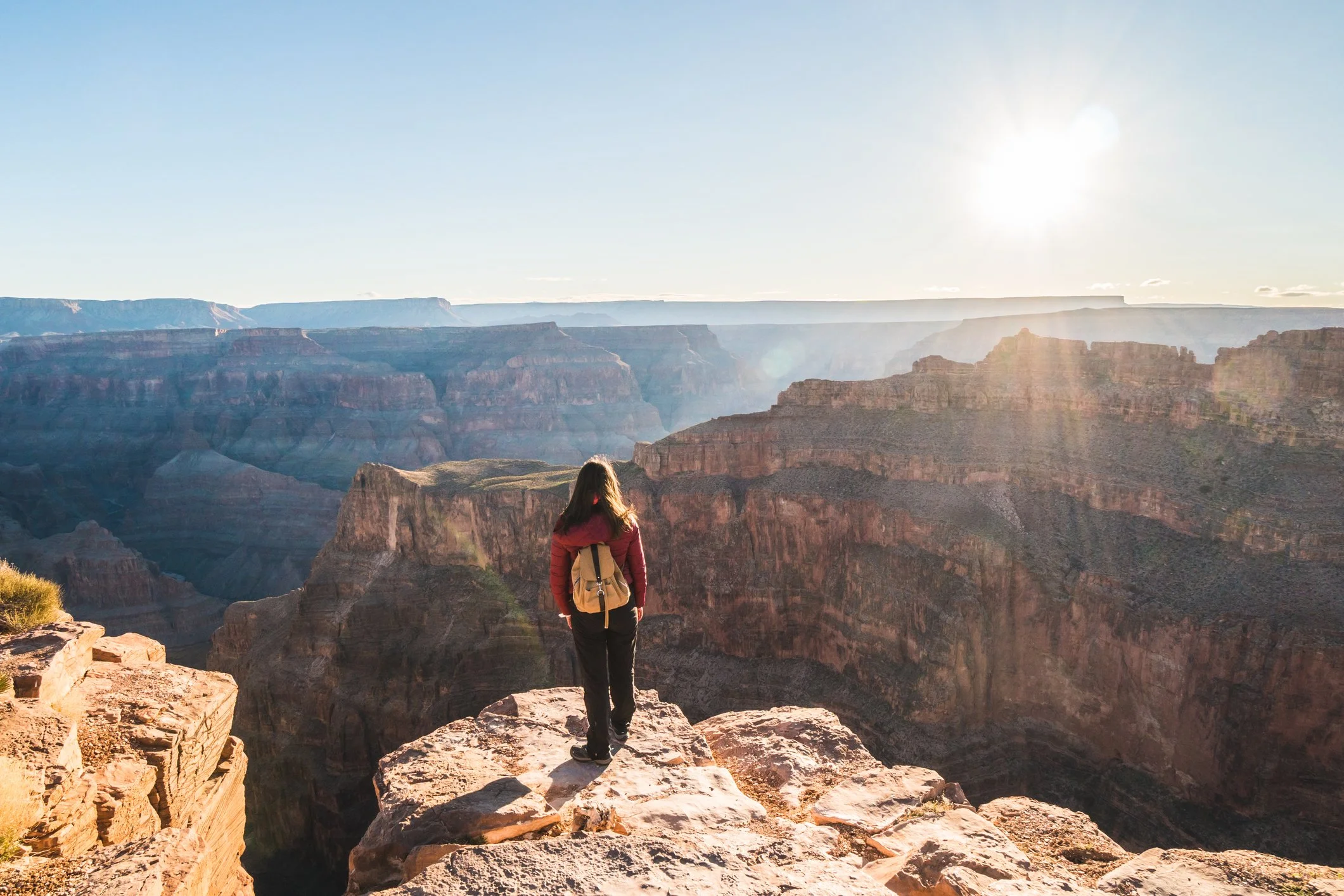 A person standing on the edge of a rocky cliff overlooking the Grand Canyon at sunset.