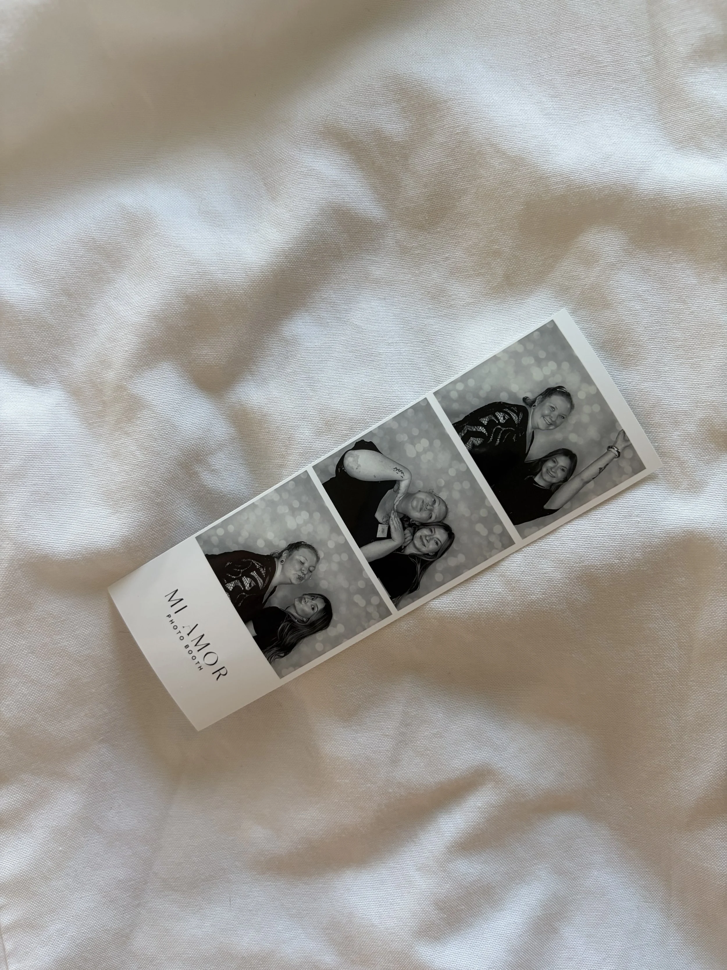 A printed photo booth strip featuring black and white photos of people, laid on a light, textured fabric.