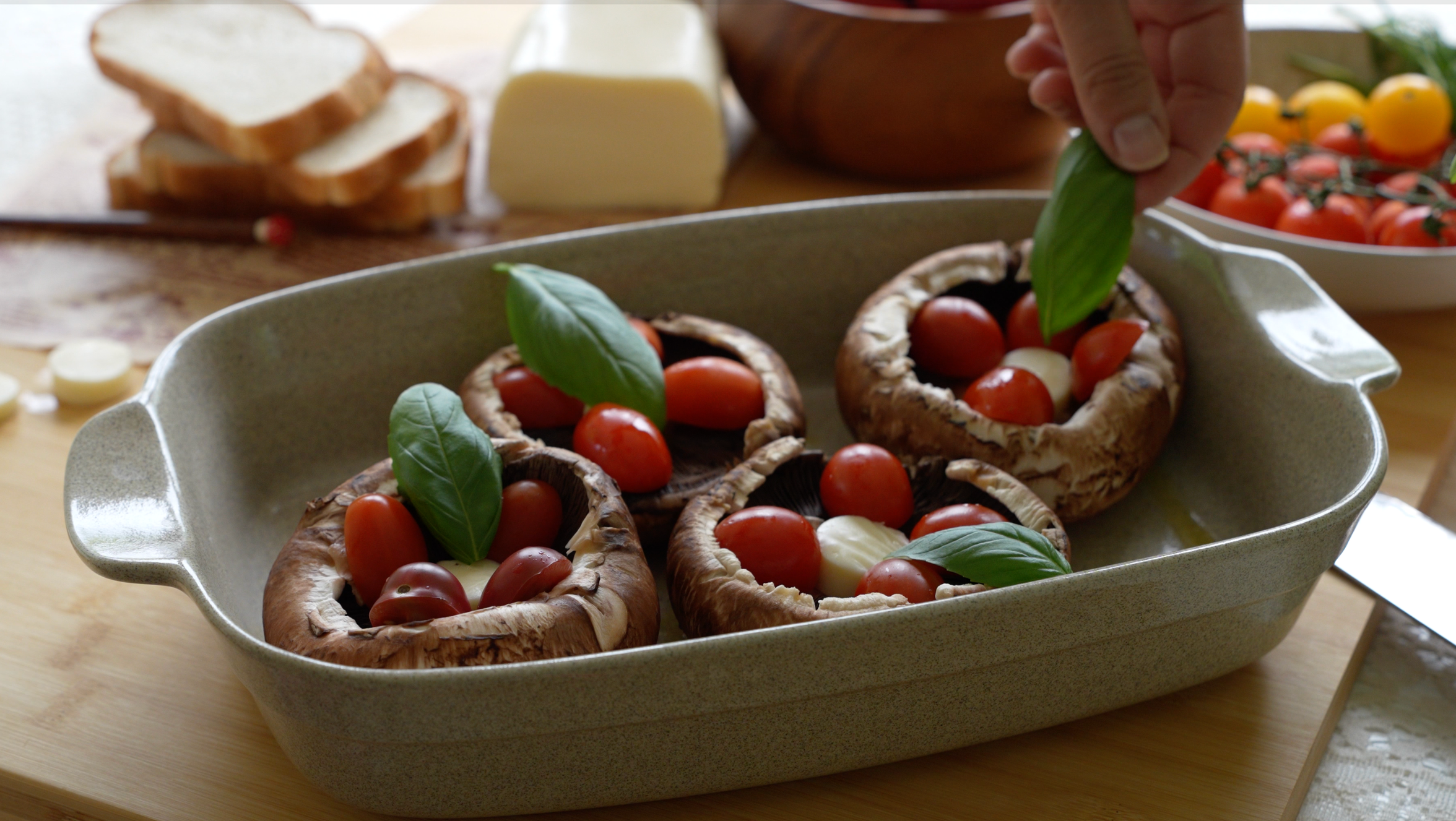 Stuffed portobello mushrooms topped with cherry tomatoes, mozzarella, and fresh basil leaves in a baking dish on a wooden table.