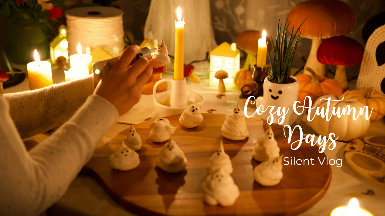 A cozy autumn-themed table with small pumpkin desserts, candles, and decorative mushrooms, featuring a person decorating the treats with a piping bag, accompanied by label 'Cozy Autumn Days Silent Vlog'.