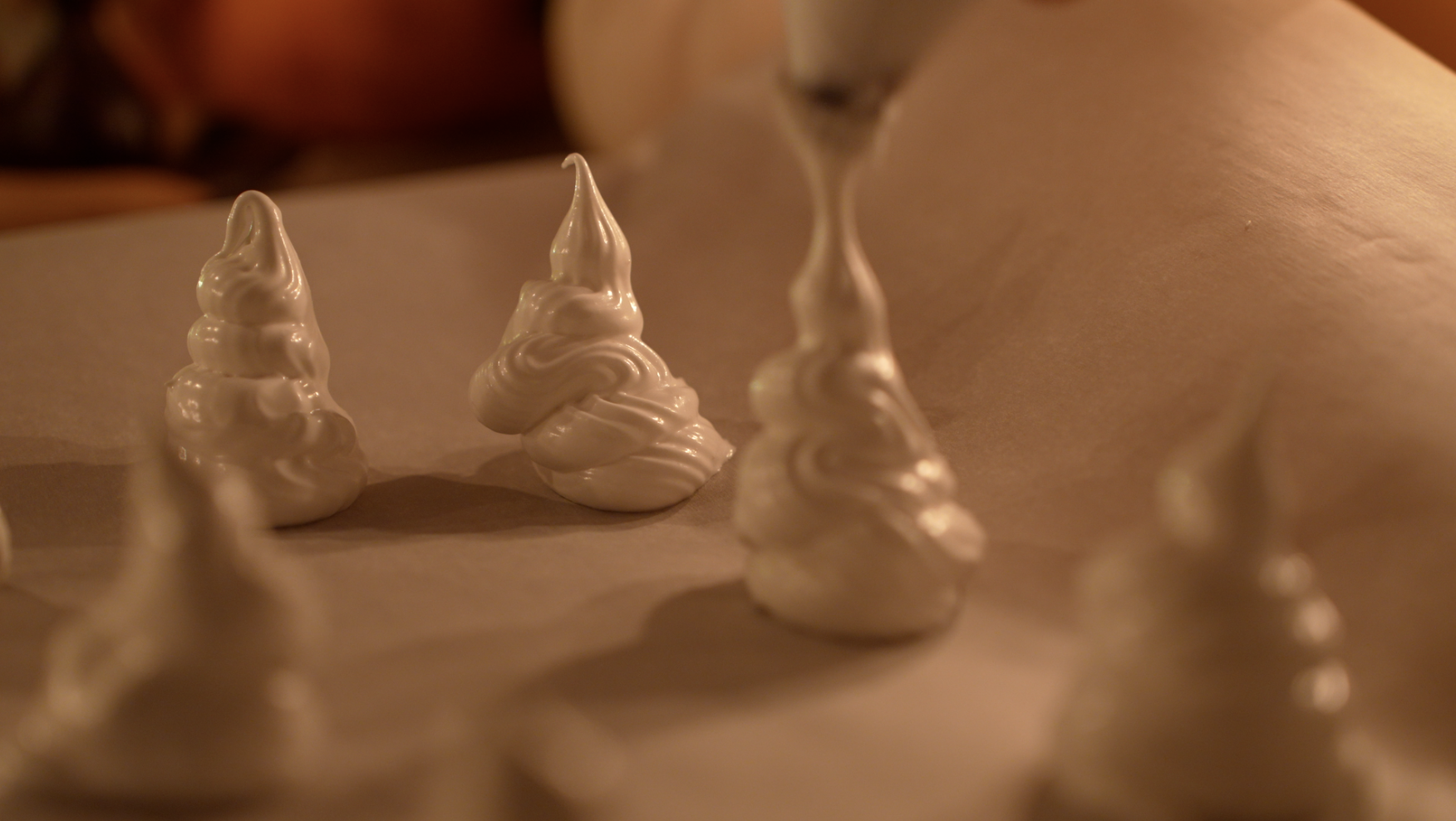 Several small, white, swirled meringue cookies on parchment paper, with a blurred background.