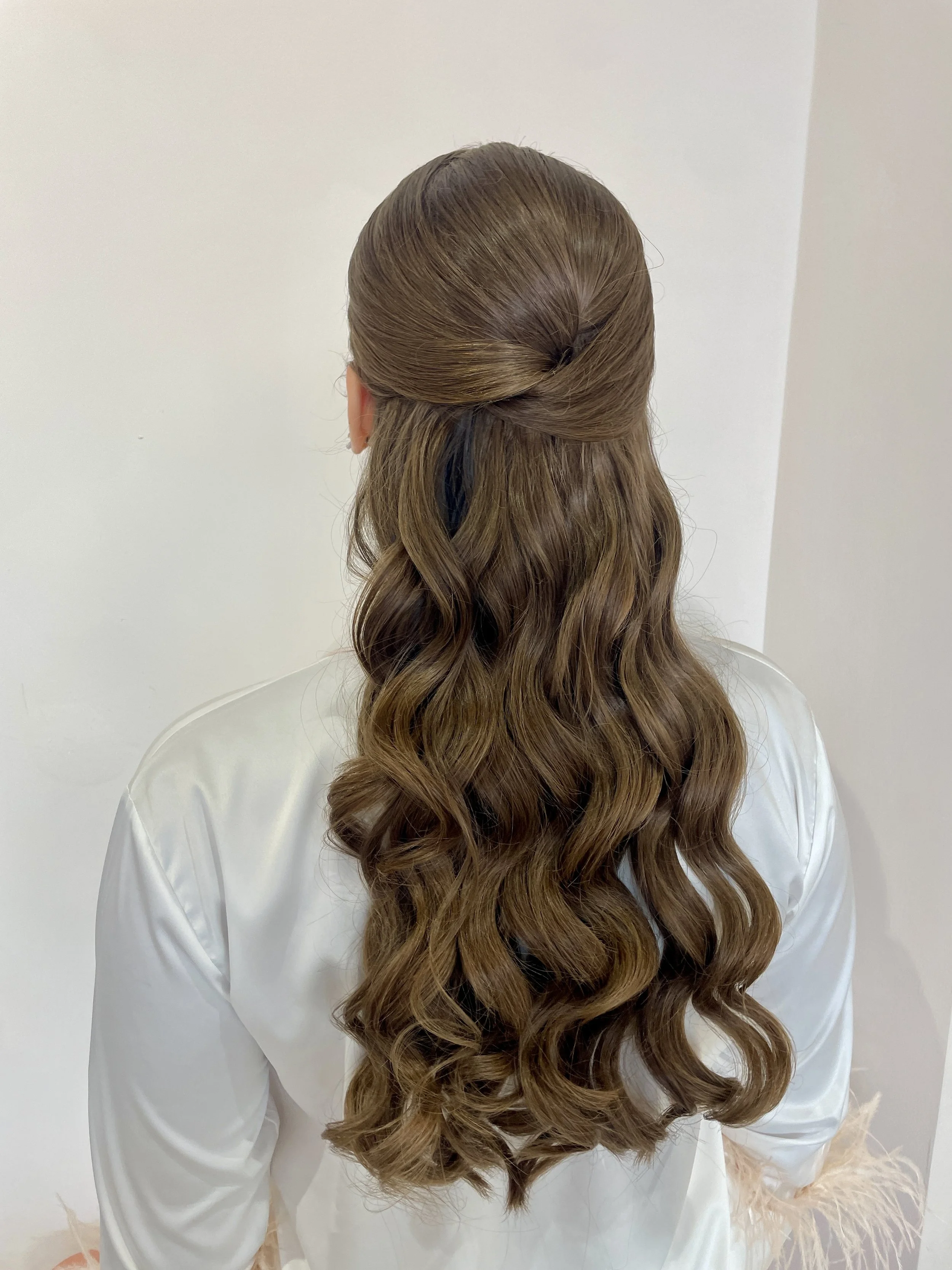 Back view of a woman with styled brown wavy hair, wearing a light-colored satin or silk robe.