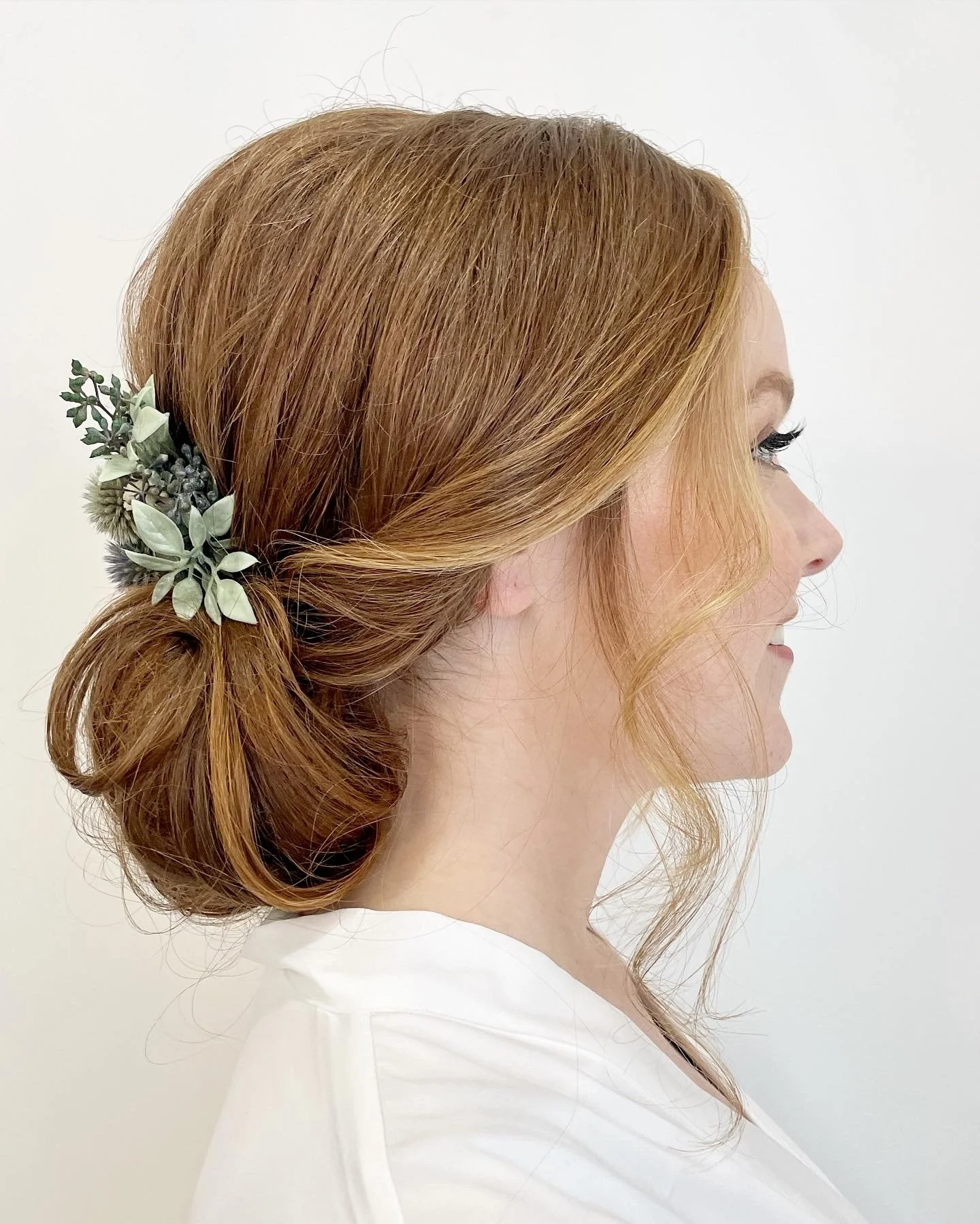 Side profile of a woman with red hair styled in a low, twisted bun with a floral hair accessory.