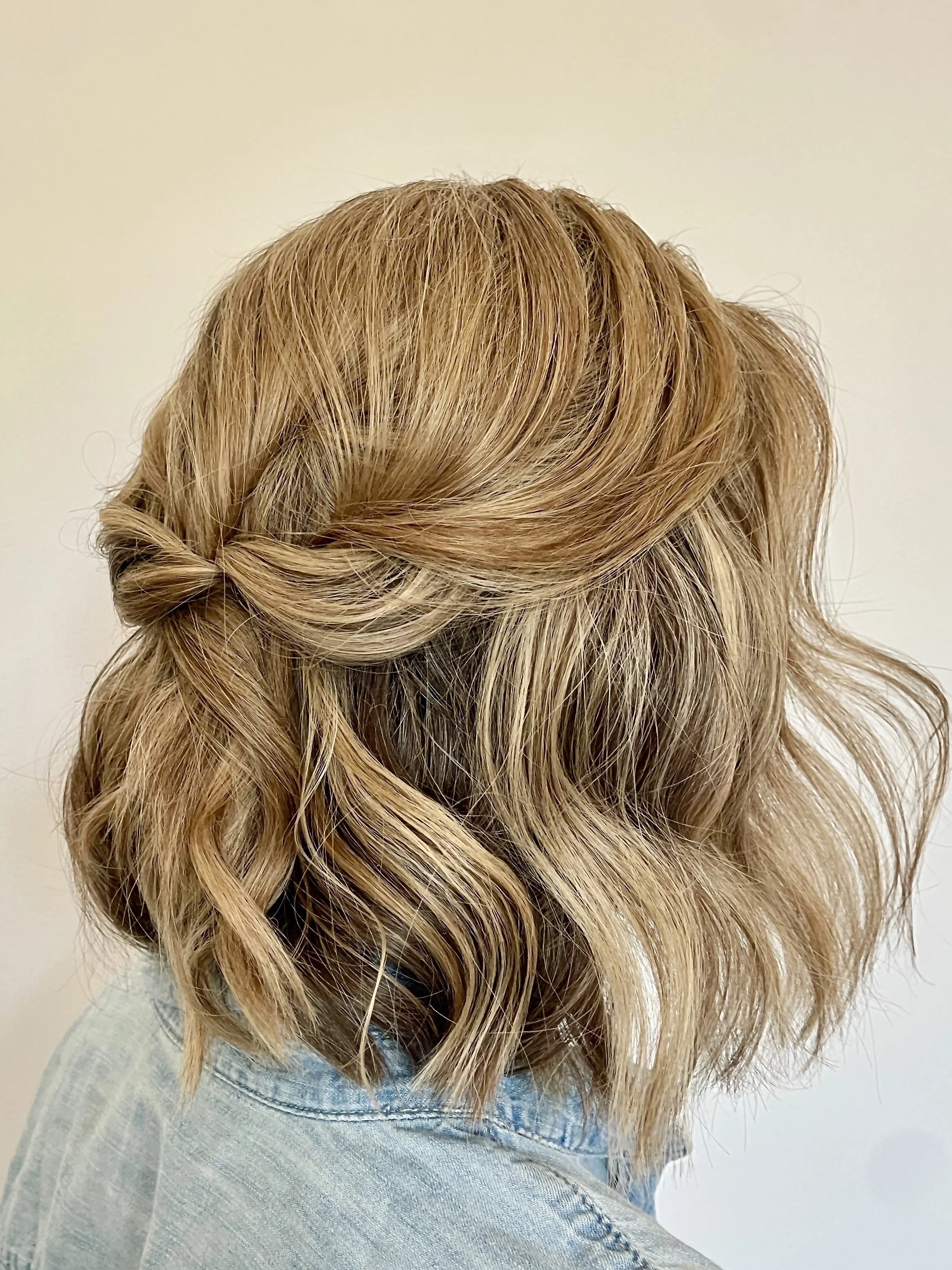 A woman with shoulder-length, wavy blonde hair styled in loose curls, wearing a light denim jacket.