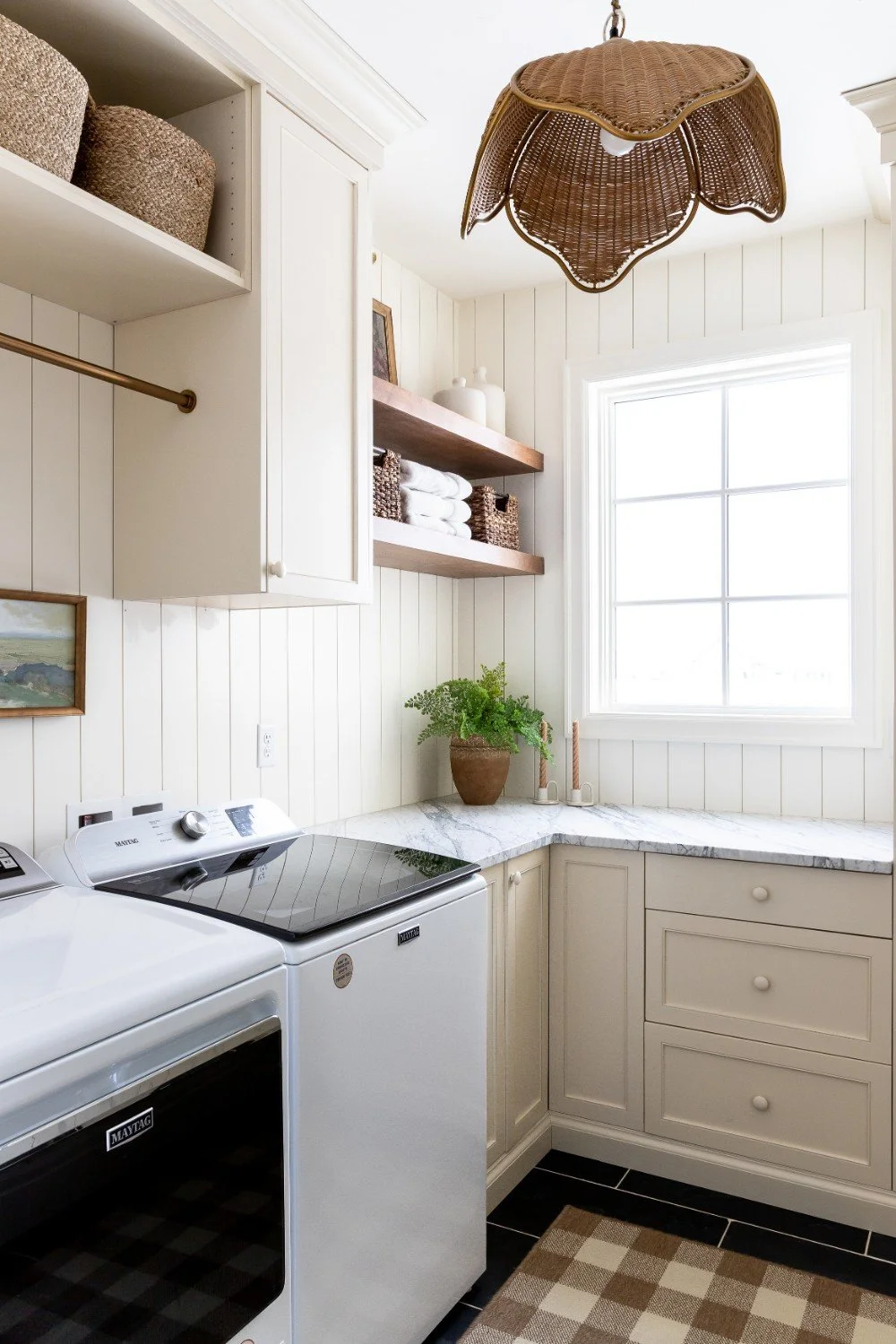 Laundry room with white cabinets, marble countertops, a window, shelves with baskets and decorative items, and a wicker ceiling light fixture.