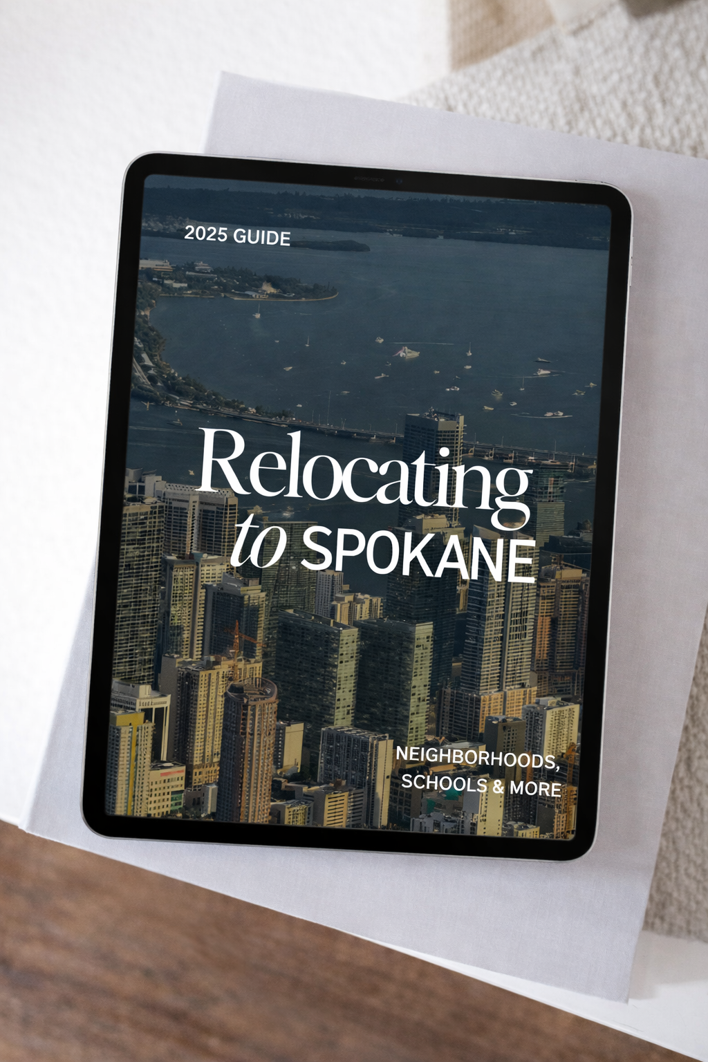 Tablet displaying a guide titled 'Relocating to Spokane' with an aerial view of a city's skyline and the water nearby, labeled as '2025 GUIDE'.