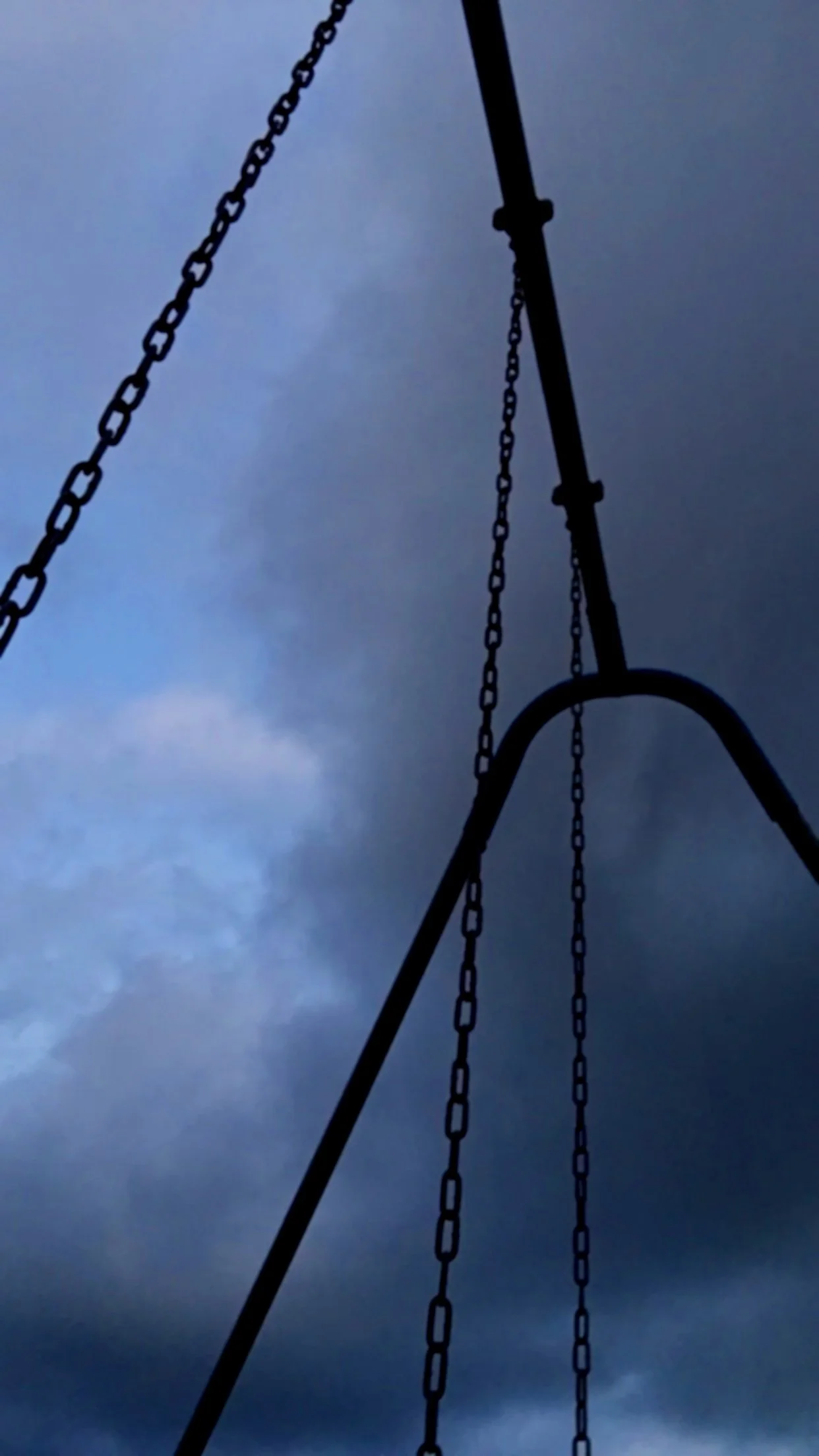 Chains hanging from a swing set frame against a cloudy, overcast sky.