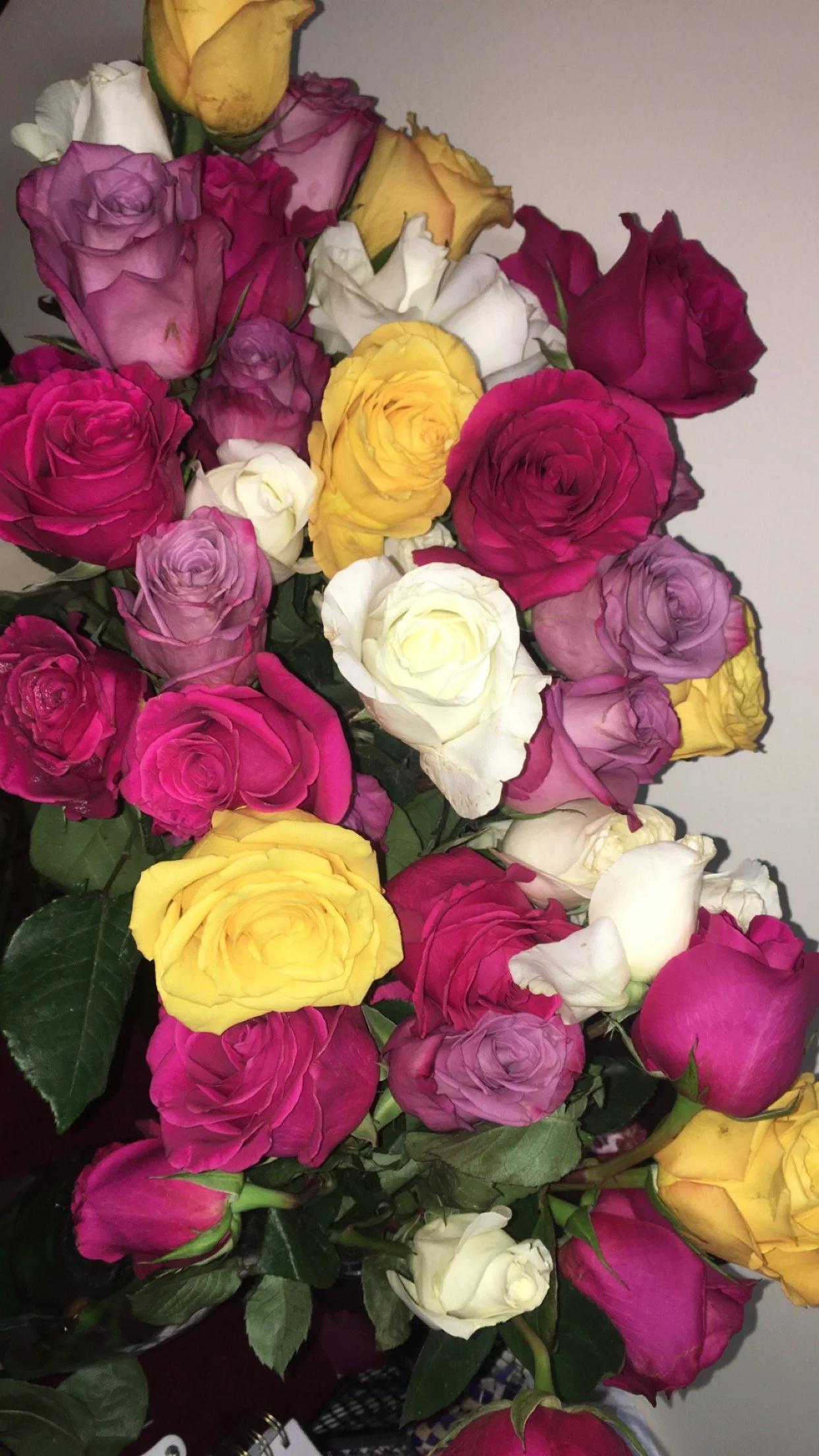 A bouquet of multicolored roses including pink, yellow, white, and purple blooms, with green leaves.