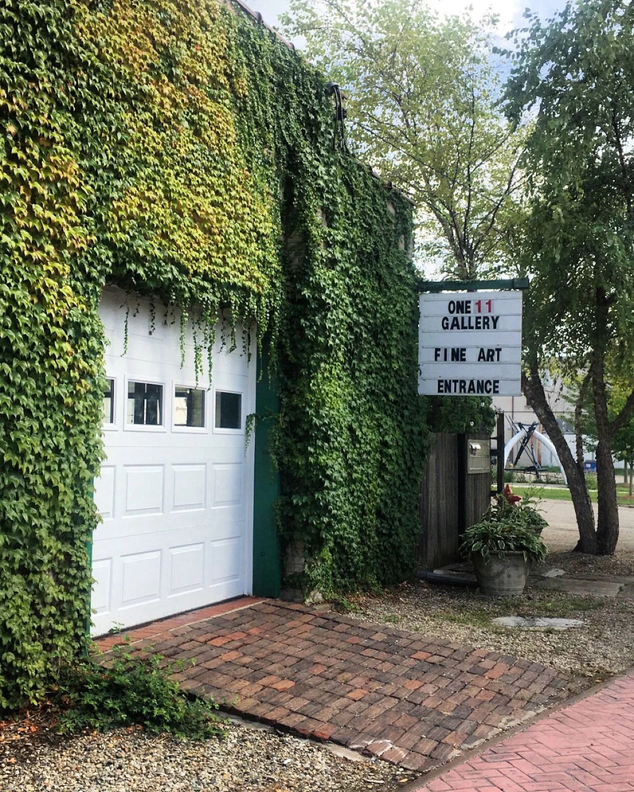Sign outside a gallery building with ivy-covered walls, reading 'One 11 Gallery, Fine Art, Entrance'.