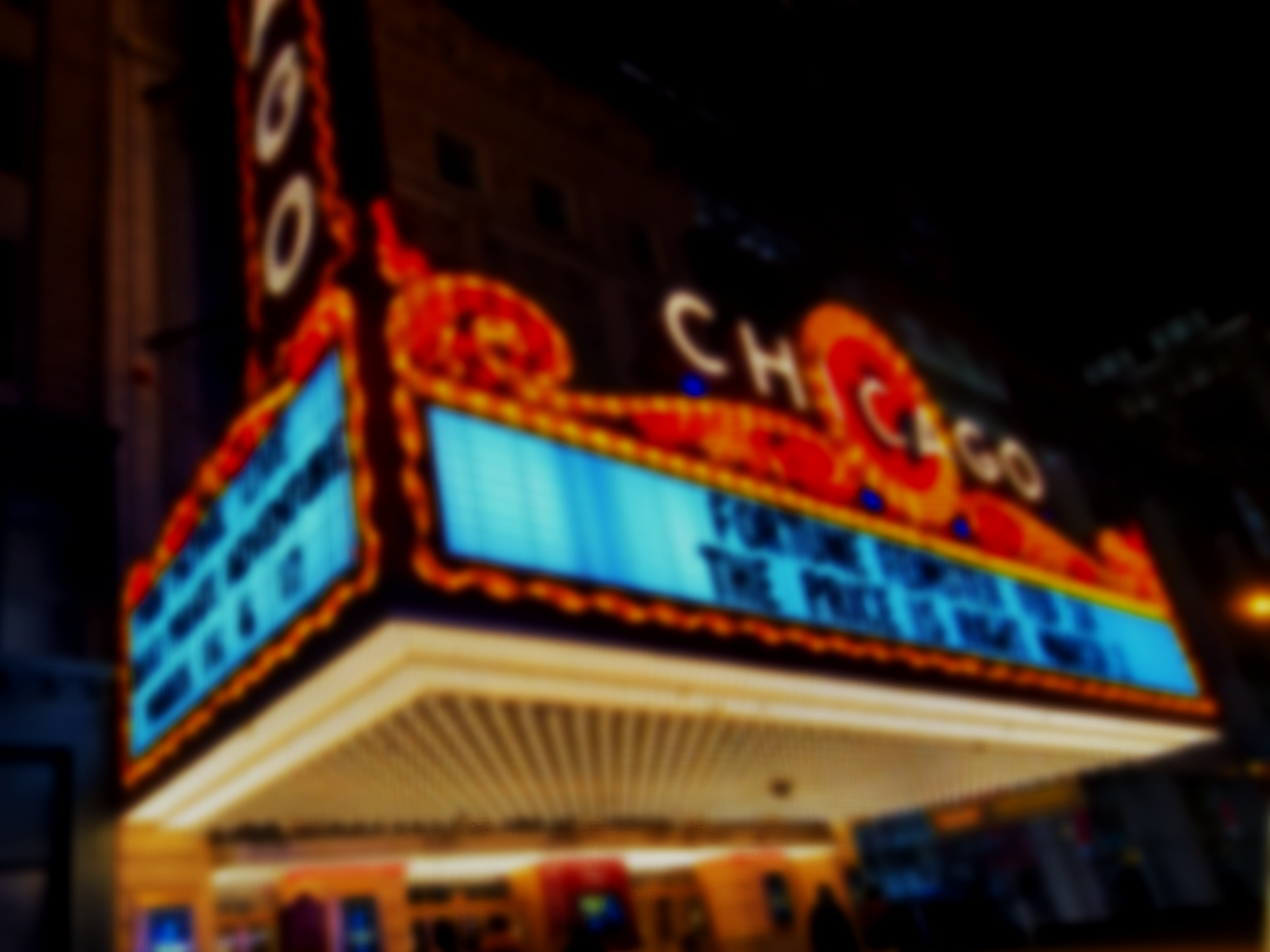 Neon-lit marquee sign of the Chicago Theater at night, with the theater's name and an animated display area.