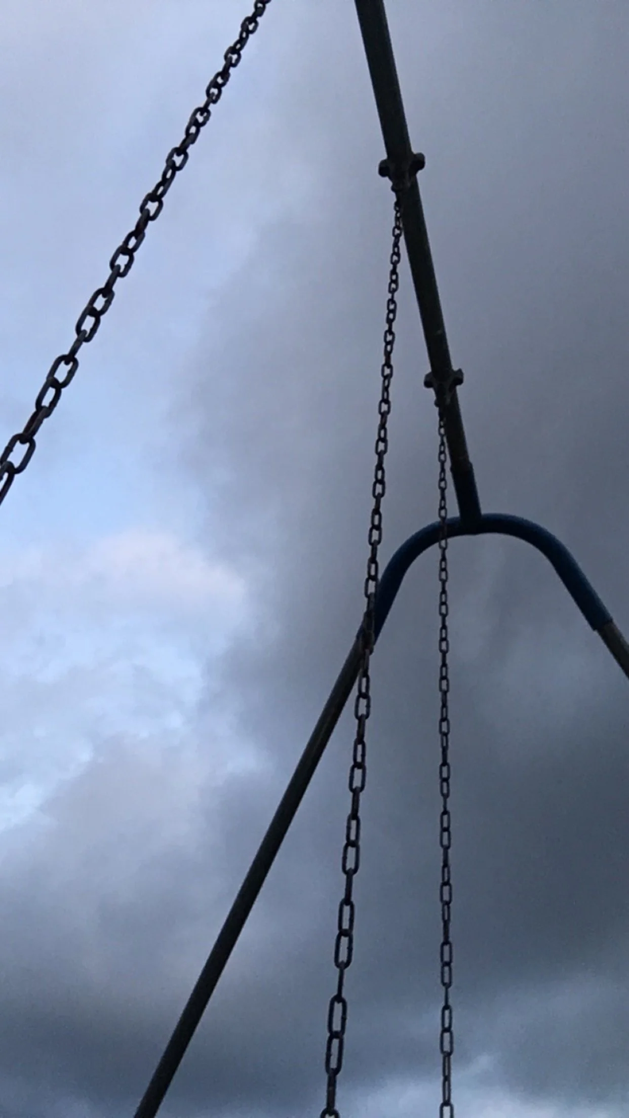 A playground swing set with empty swings and dark, cloudy sky