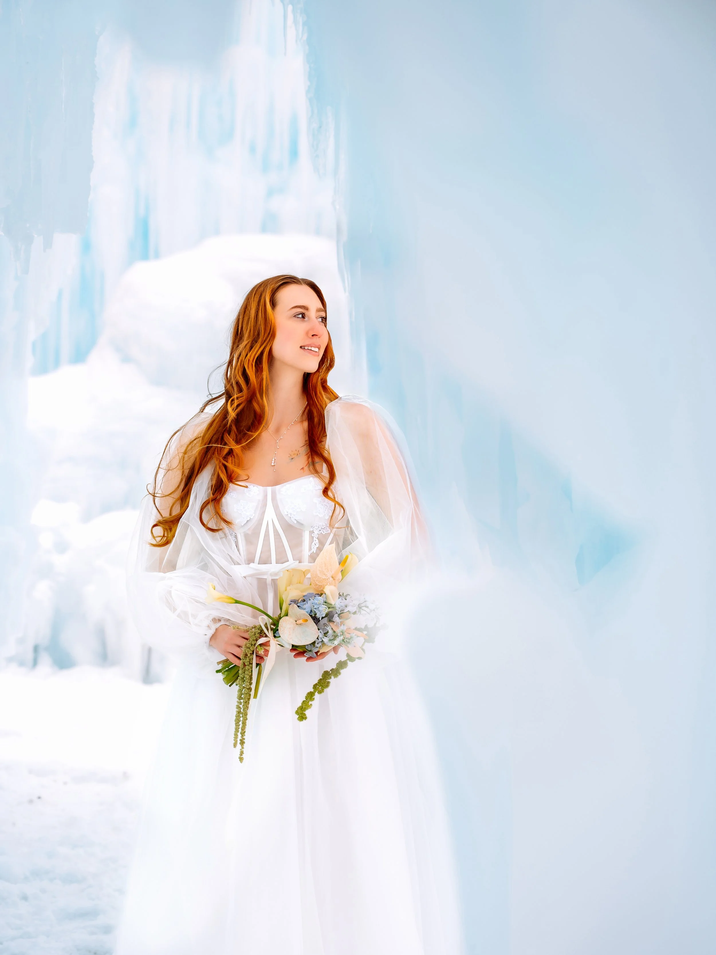 A woman with long red hair in a white wedding dress holding a bouquet of flowers in a snowy, icy environment with blue ice formations.