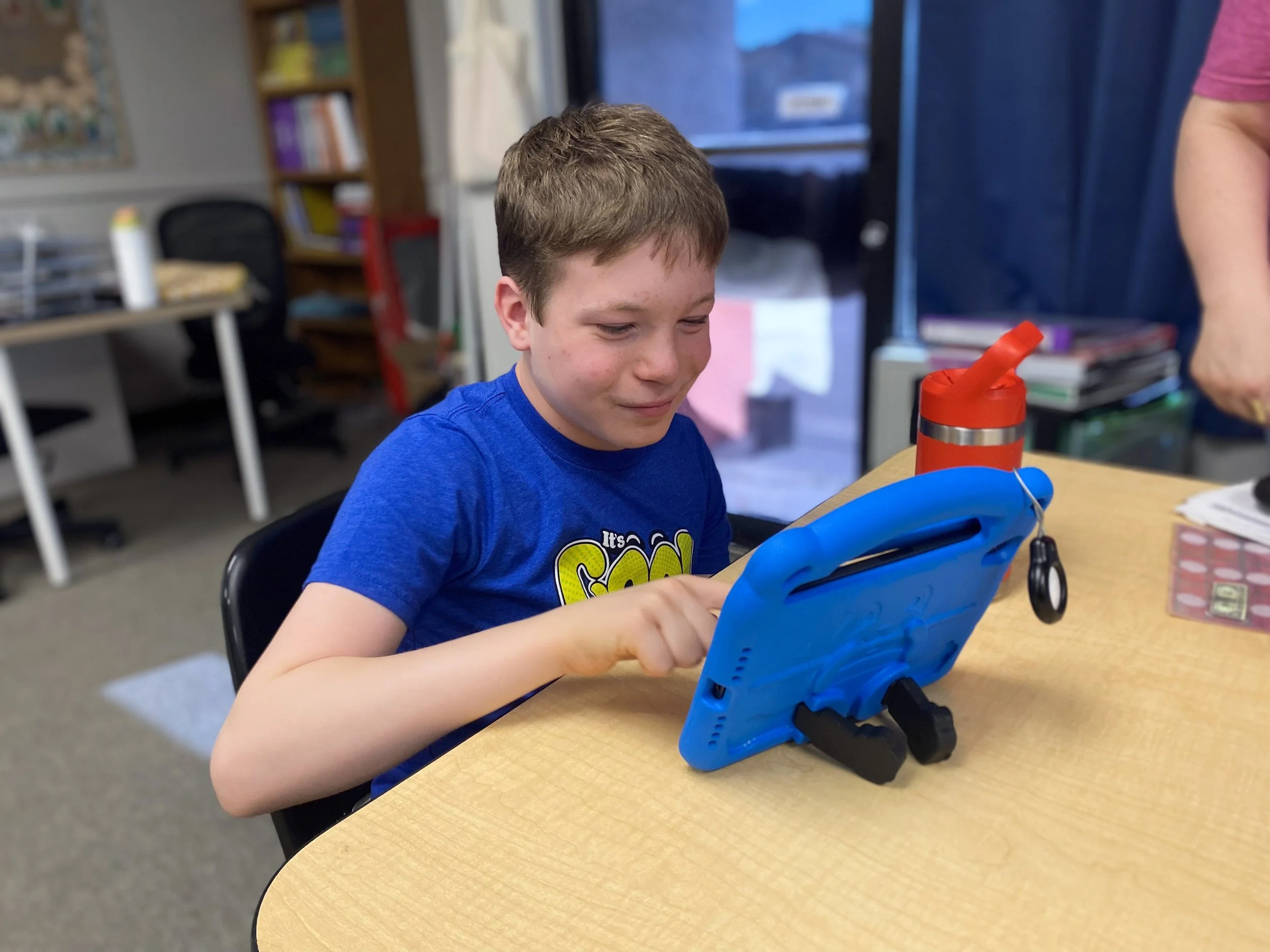A young boy in a blue T-shirt sitting at a wooden table. K-12 autism academy in Chandler, Arizona