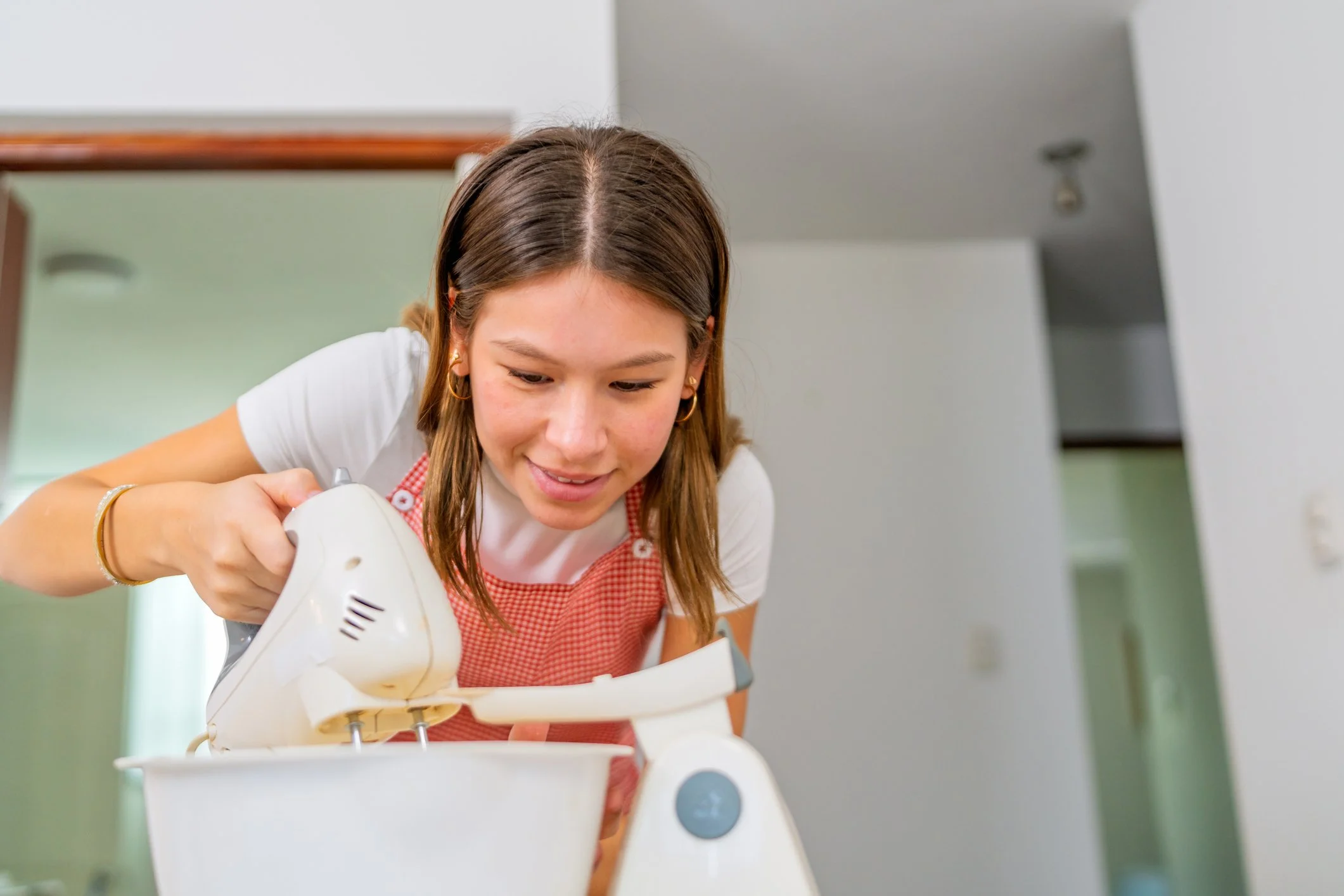 Young woman mixing batter in a white bowl with a hand mixer in a kitchen. Vocational and life skill training at Story Autism in Chandler, Arizona
