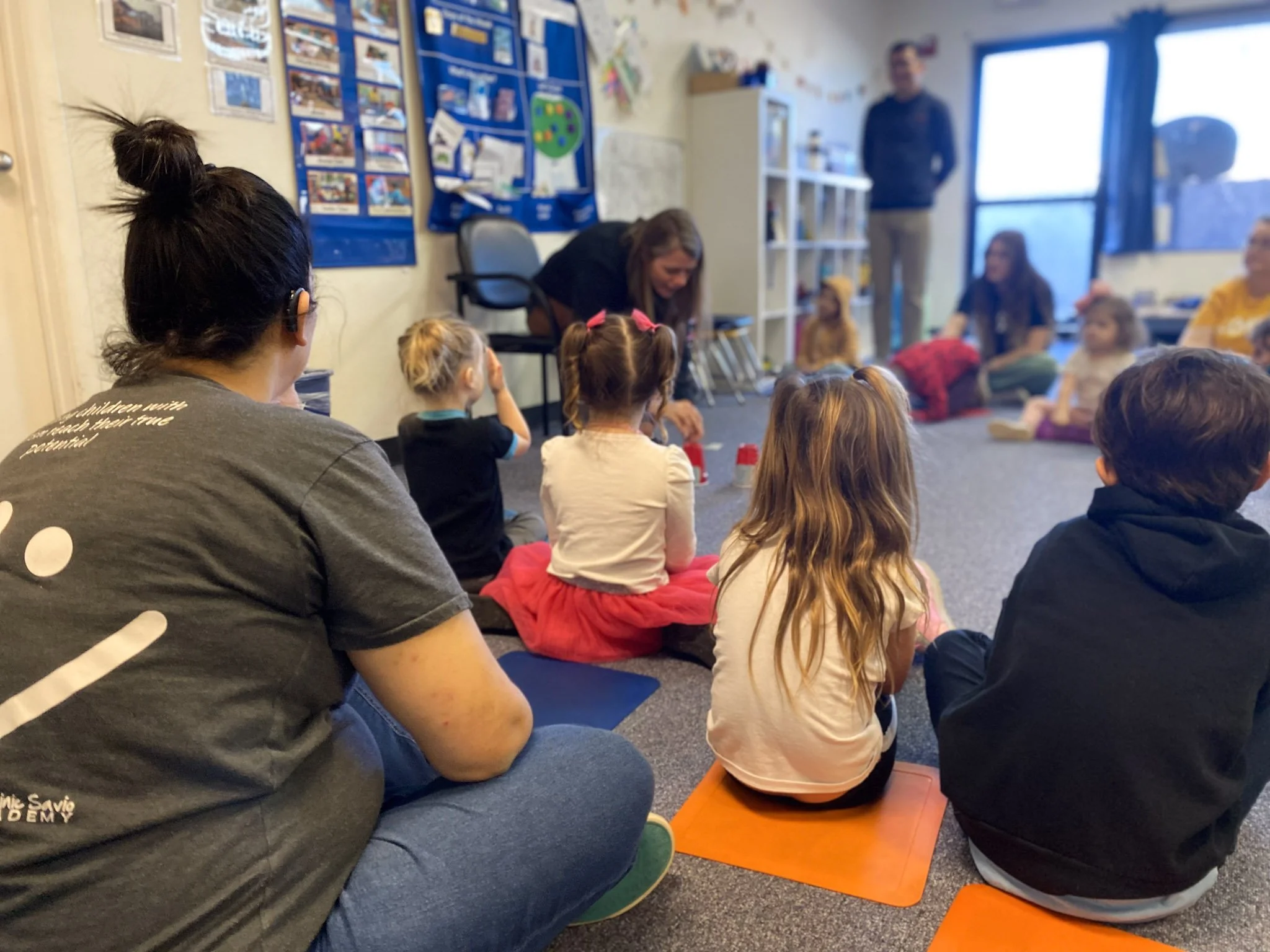 Children and adults seated on the floor in a classroom, participating in a group activity. Inclusive pre-school Chandler, Arizona