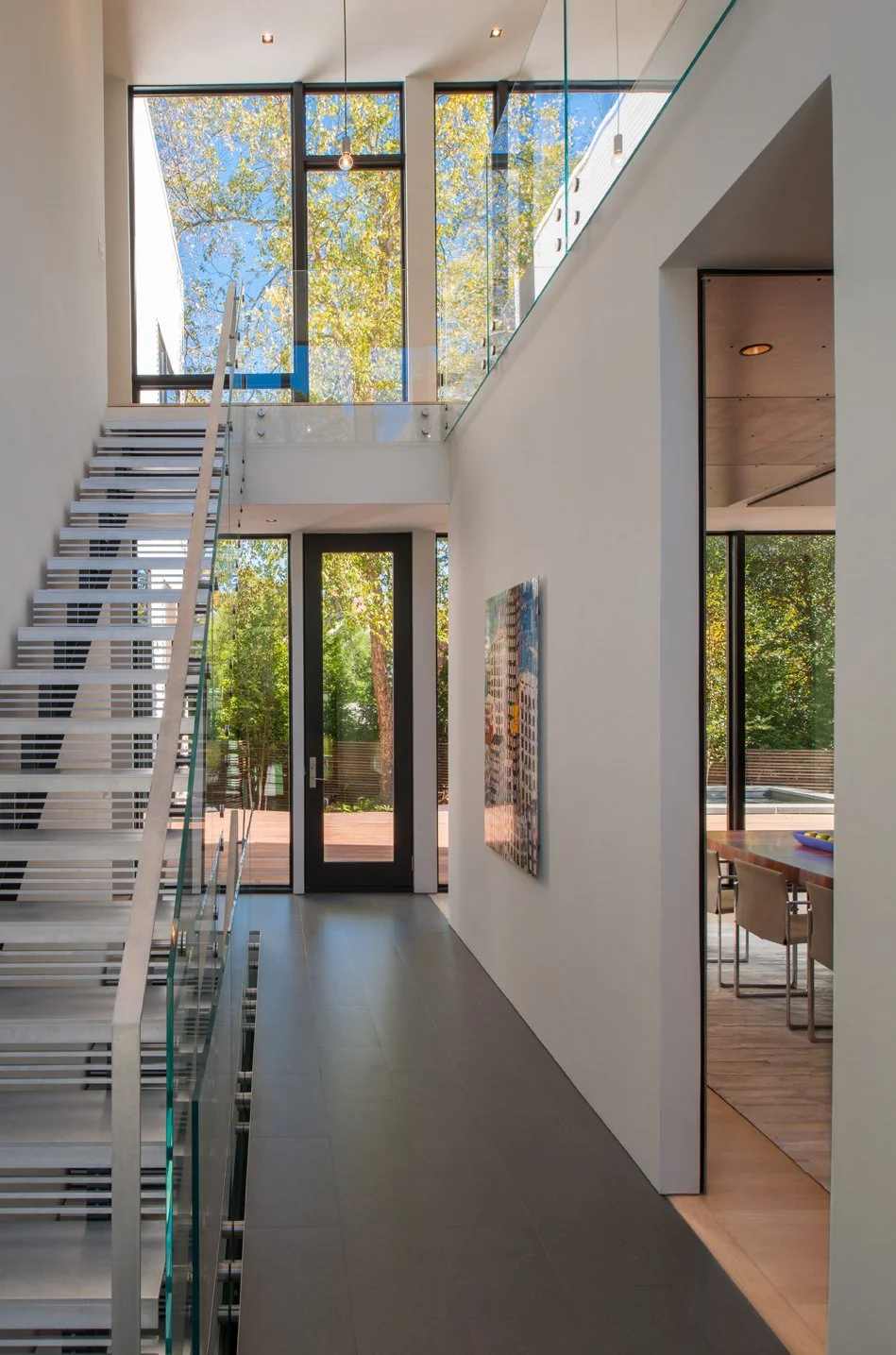Modern interior home with a staircase, large windows, and dining area visible through an open doorway.