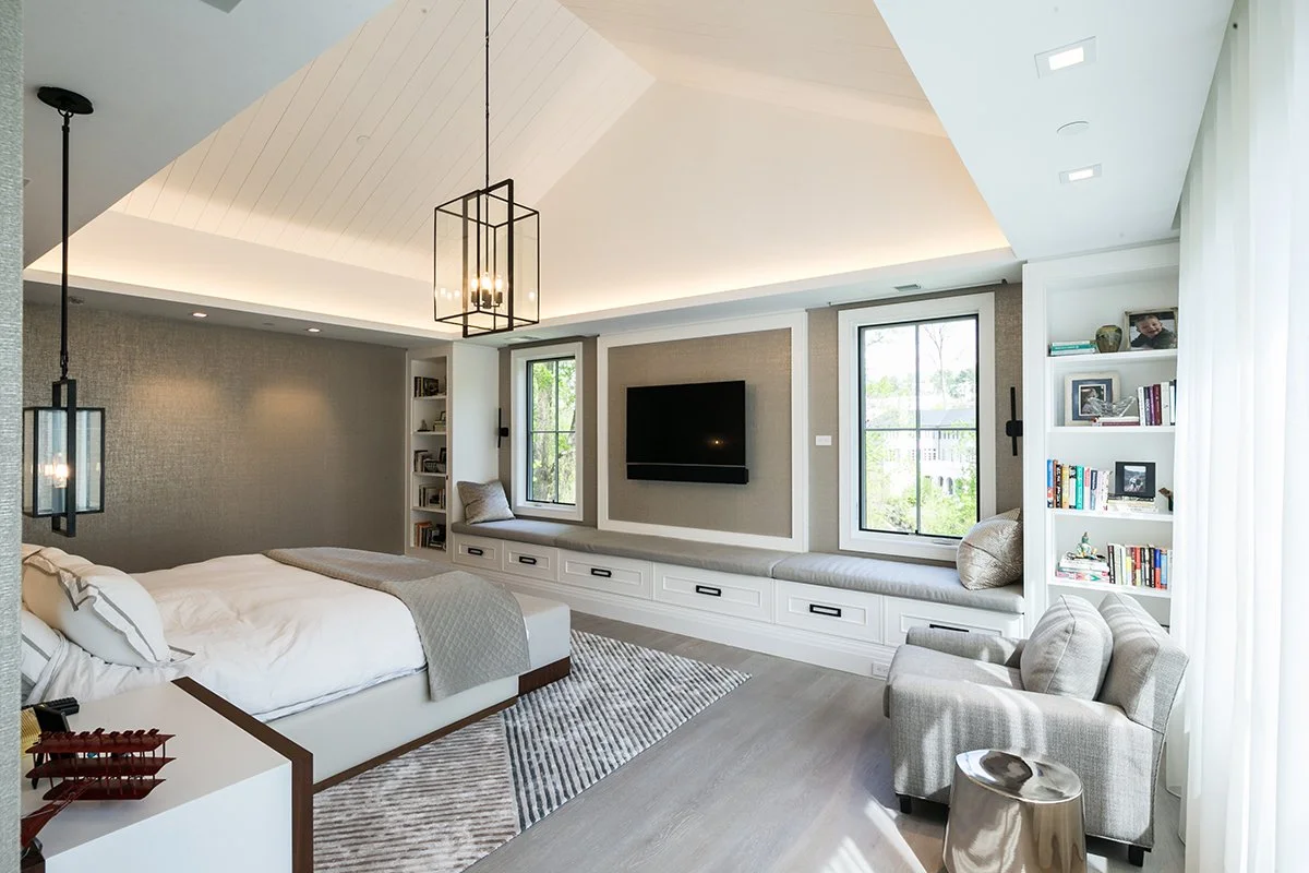 Bright modern bedroom with a bed, built-in window seat with storage, TV, and bookshelves.