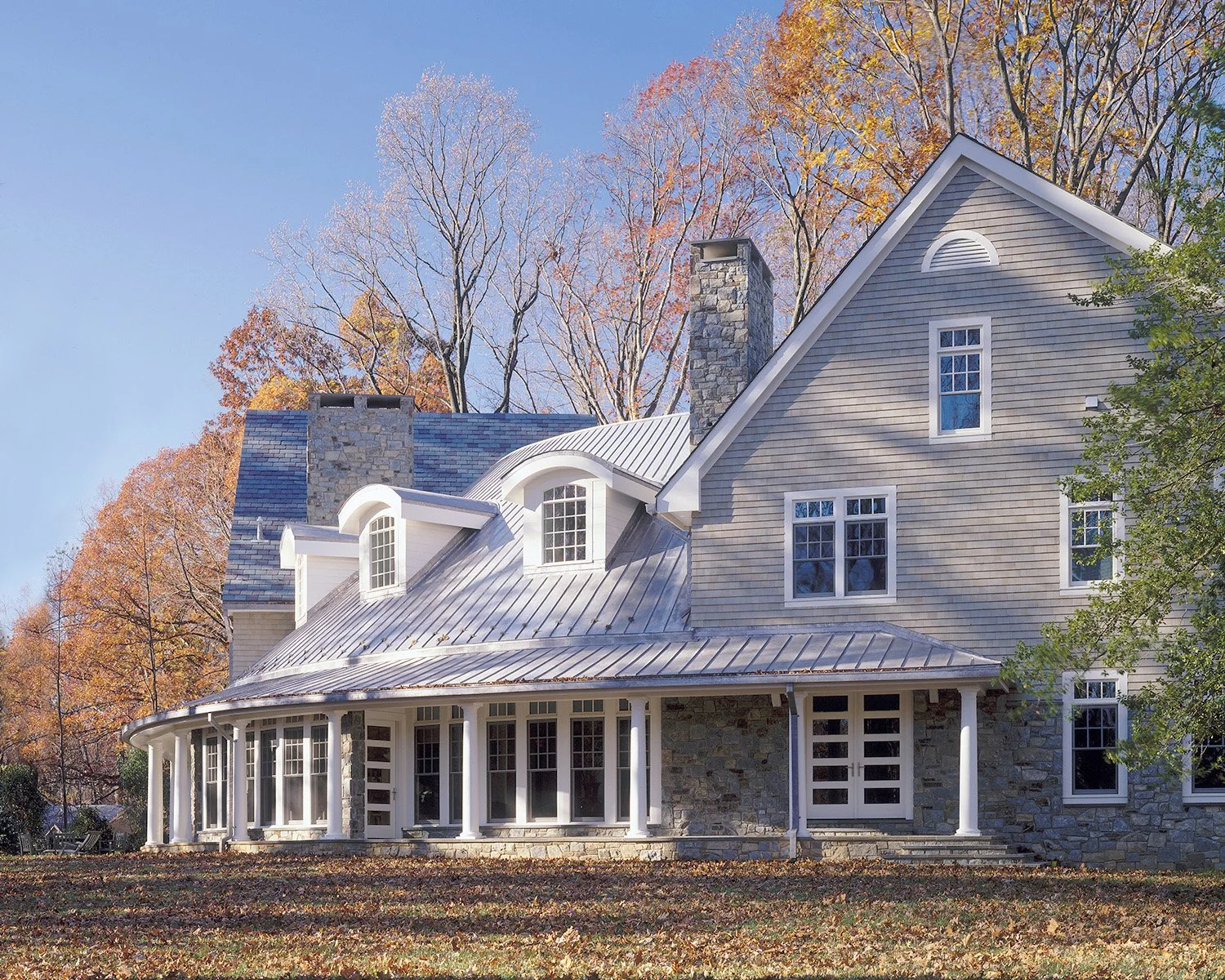 A large house with a combination of stone and siding exterior, multiple chimneys, and slate roofing, surrounded by autumn trees.
