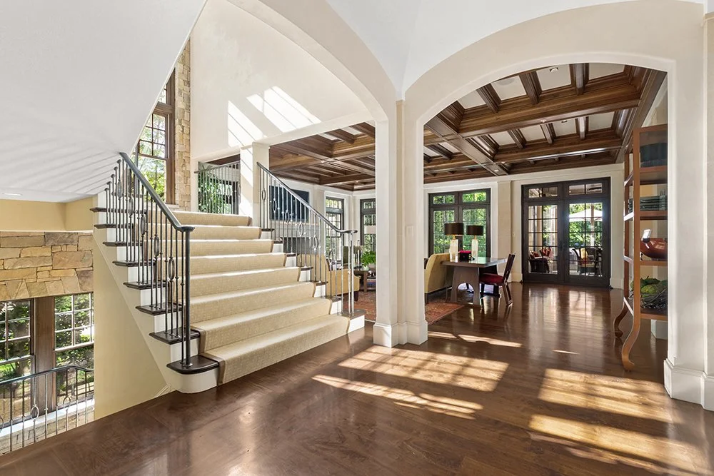 Interior of a bright, spacious house with a staircase, wooden ceiling, large windows, and a sitting area.