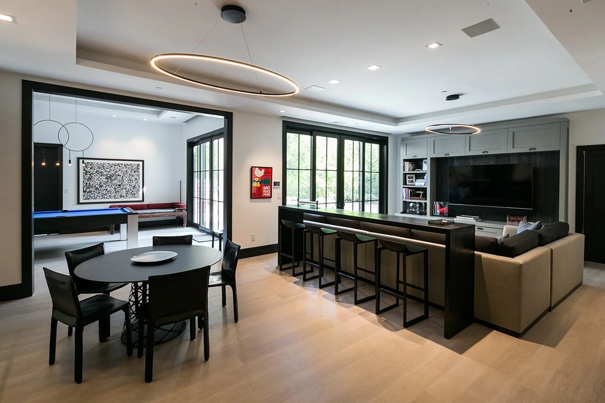 Modern open-concept living room and dining area with a bar, a sectional sofa, large windows, and contemporary light fixtures.