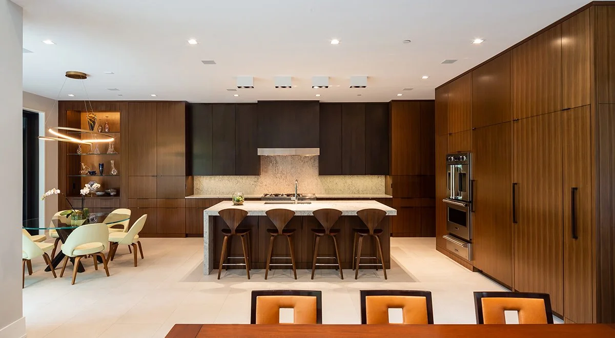 Modern kitchen with wooden cabinets, a marble island, and five bar stools, with dining chairs visible in the foreground.