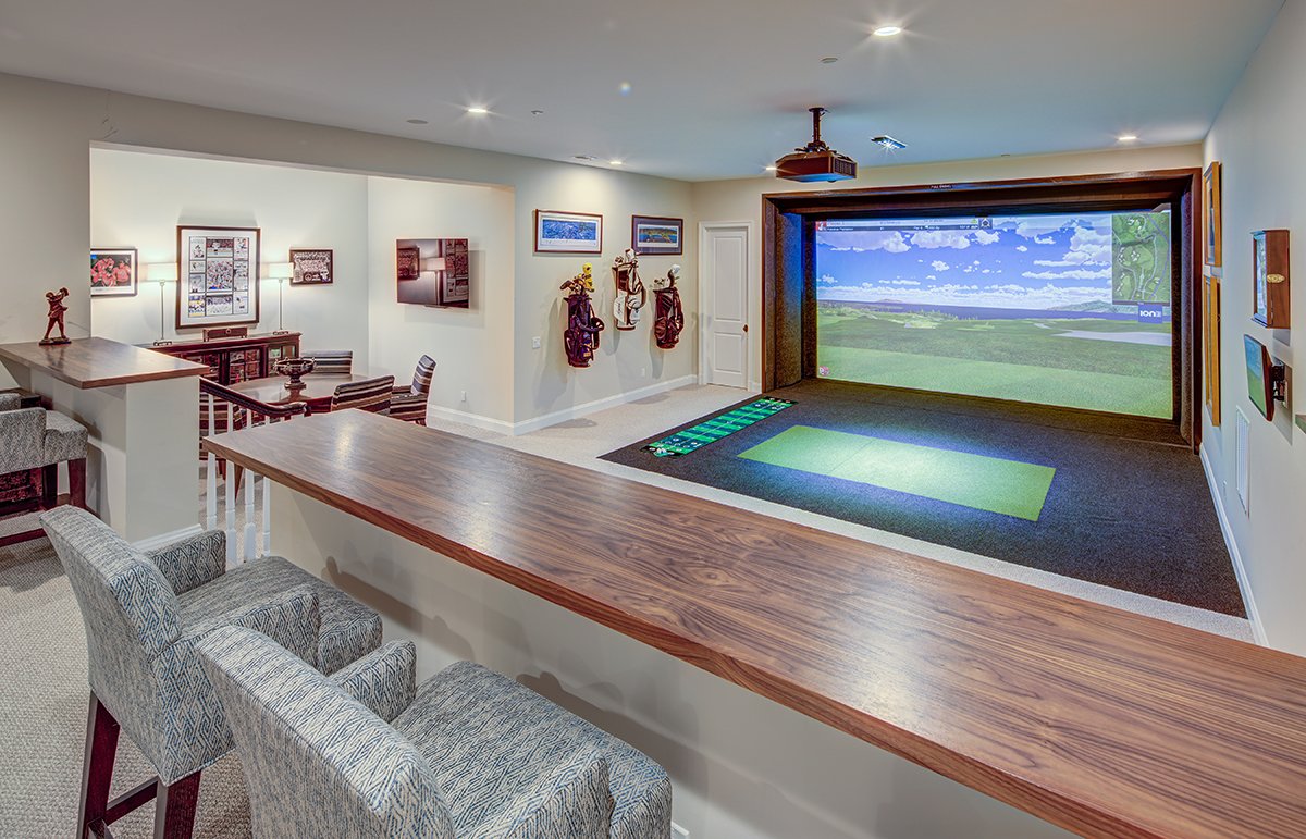 A spacious basement with a golf simulator, seating area, and artwork on the walls.