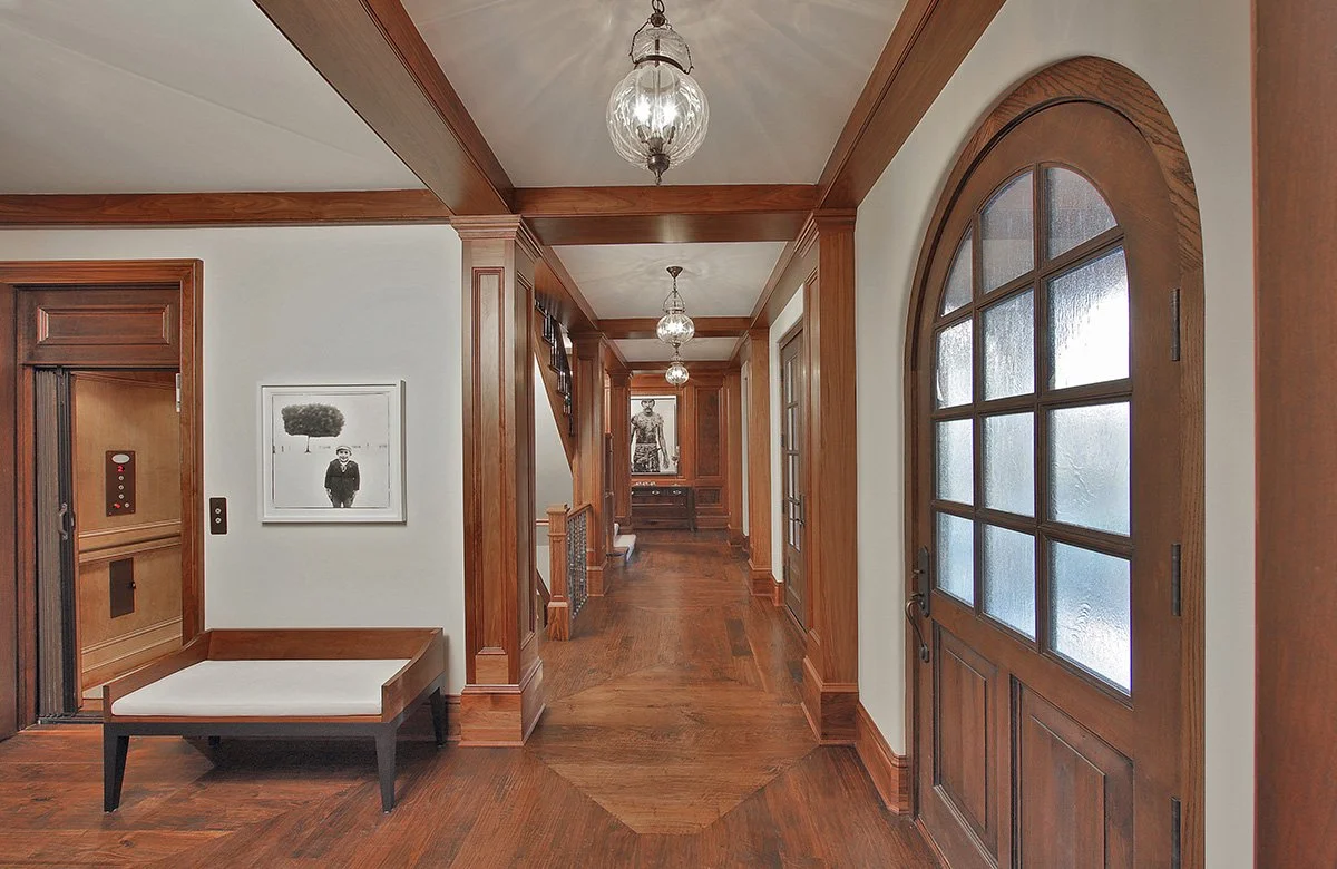 Hallway with wooden walls and flooring, frosted glass door on the right, artwork on the wall, and vintage-style hanging light fixtures.
