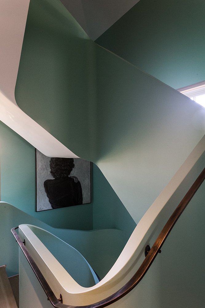 Interior of a teal-colored staircase with a wooden handrail and a black-and-white portrait of a woman on the wall.