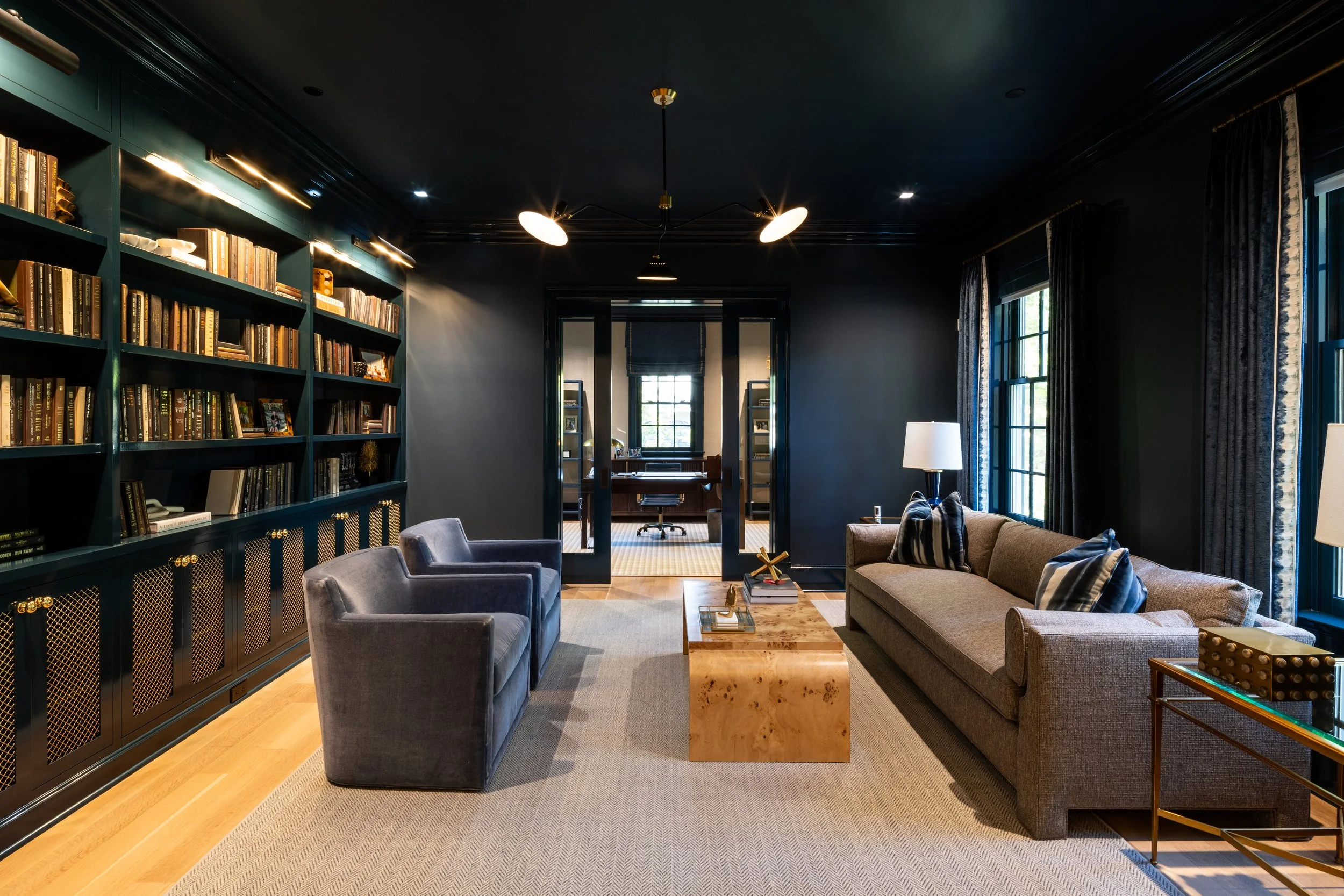 Living room with dark walls, large windows with curtains, a bookshelf, a sofa, armchairs, and a coffee table.