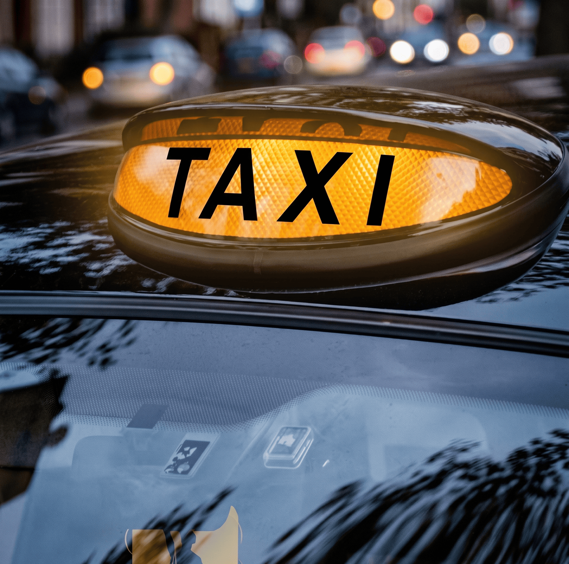 A close-up of an illuminated yellow taxi sign on the roof of a black car, with blurred city lights in the background.