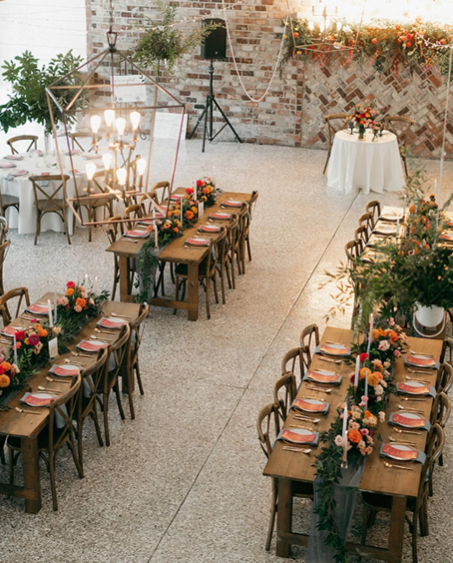 Decorated banquet hall with long wooden tables, floral centerpieces, candles, and arranged place settings for a celebration event.