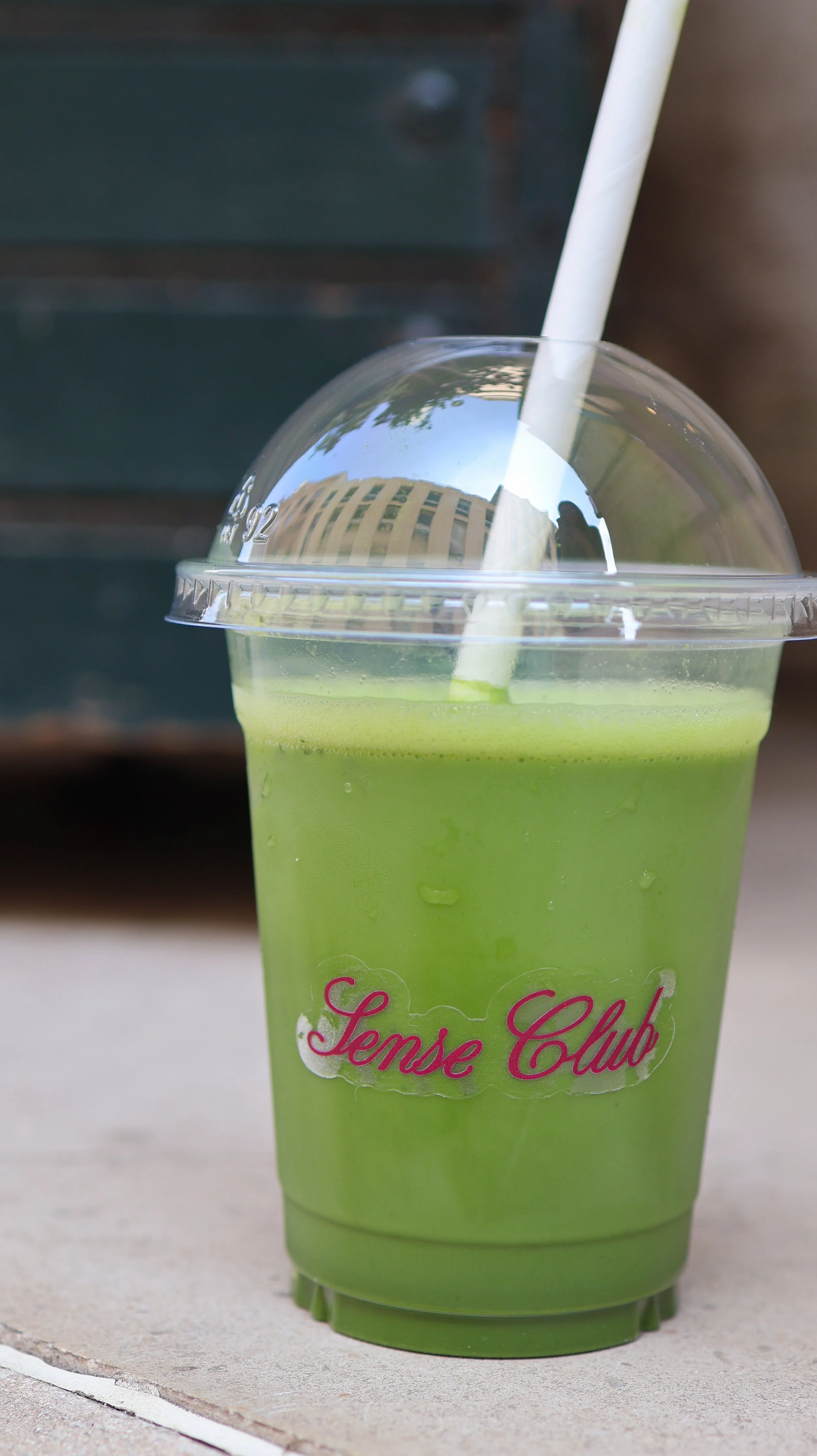 Un verre de smoothie vert avec une paille en plastique, portant une étiquette 'Sense Club'.