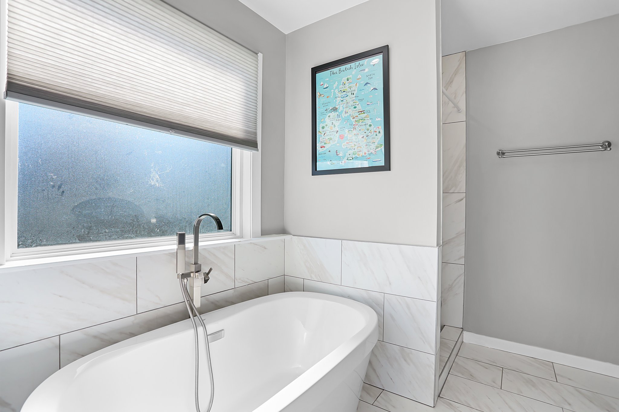 Bathroom with a window, framed map of the British Isles on the wall, bathtub, and marble tiles.