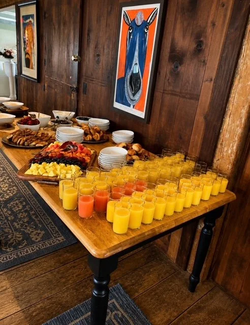 Buffet table with fruit, pastries, and glasses of orange and pink juice in a wooden-paneled room.