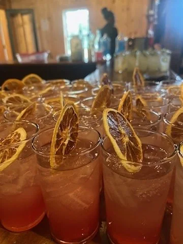Several glasses of pink lemonade with lemon slices on top, arranged on a wooden table in a bar or restaurant setting.