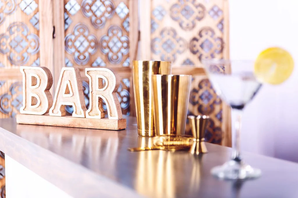 Bar setup with wooden "BAR" sign, gold bar tools, and a cocktail glass with lemon slice.