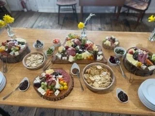 A wooden table decorated with various bowls and plates of snacks, fruit, and desserts, including sliced bread, berries, and flowers in small vases.