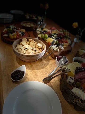 Assorted desserts and fruit platters on a wooden table, with a bowl of crackers and a small dish of jam or sauce.