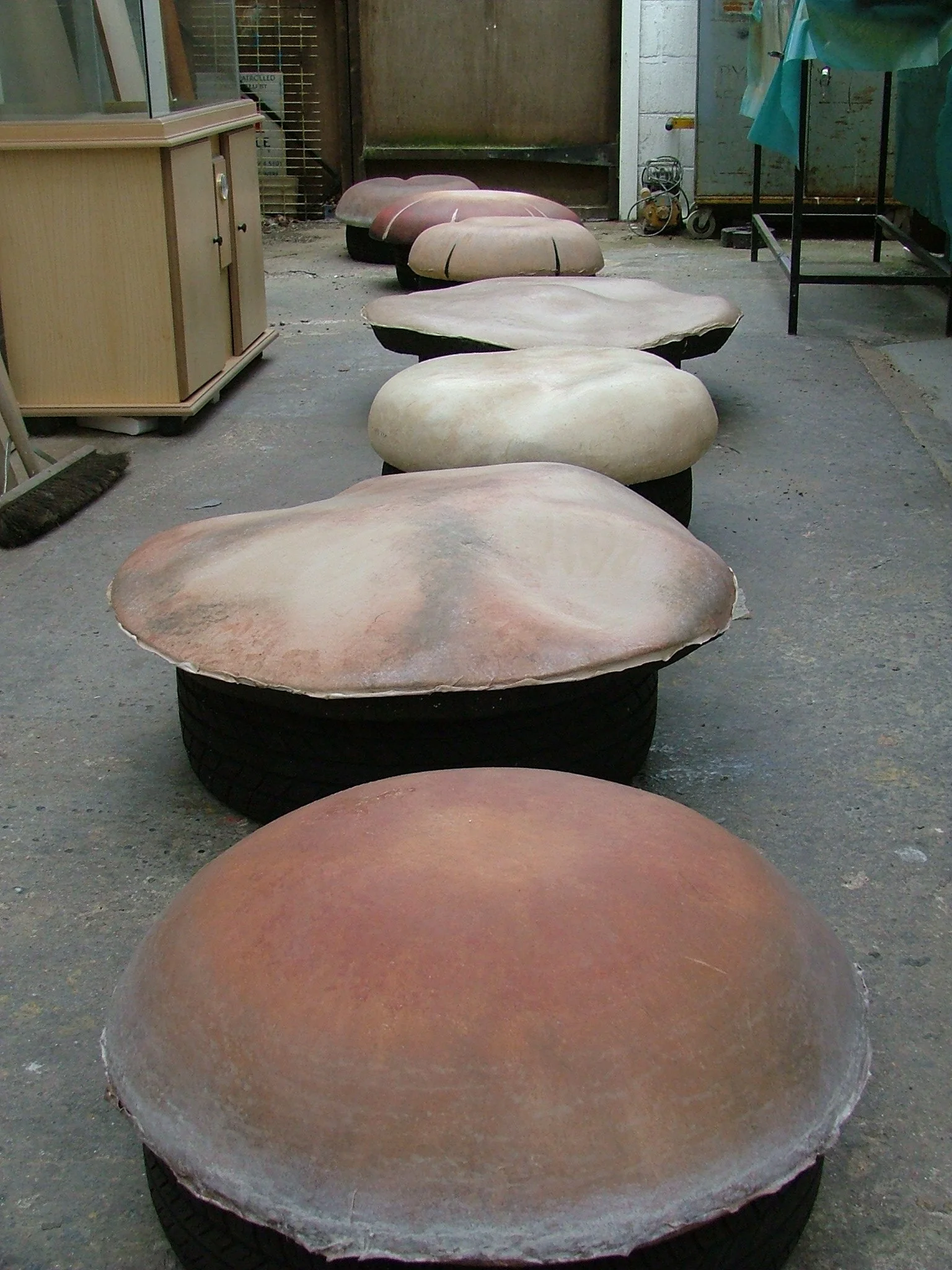 A row of large, flat, rounded stones placed on top of old tires in an outdoor workshop area.