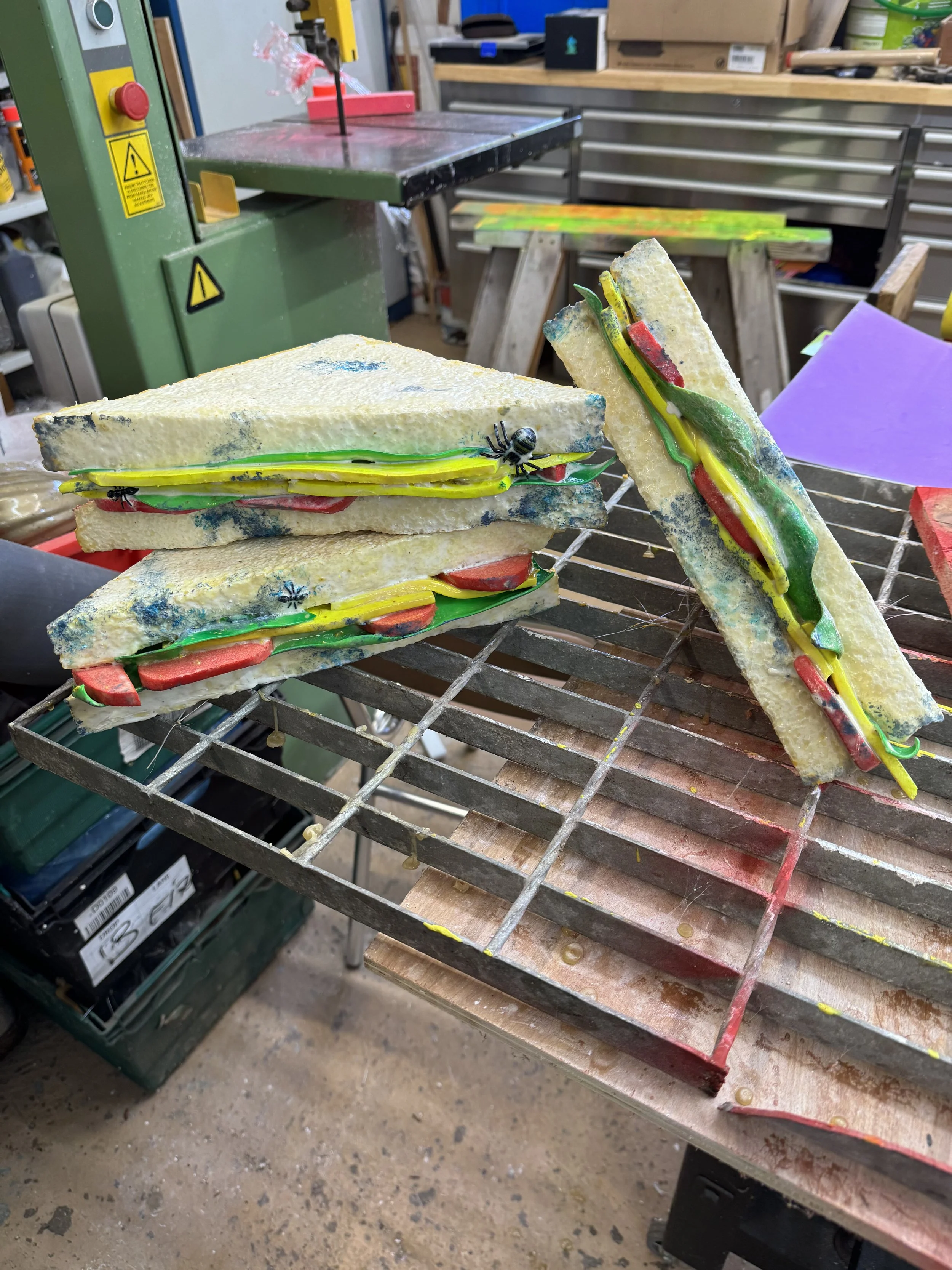 Fake oversized prop sandwiches on a metal grid in a workshop.