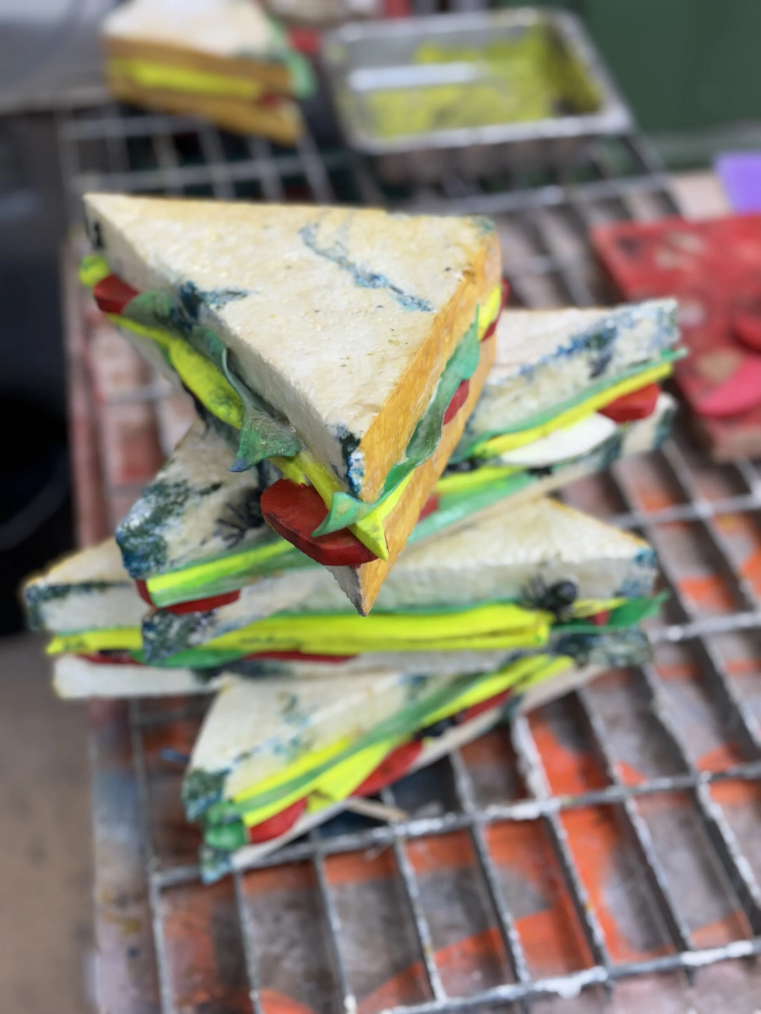 Stack of colorful, unwrapped, menacing-looking sandwich slices on a wire rack at a market or bakery.