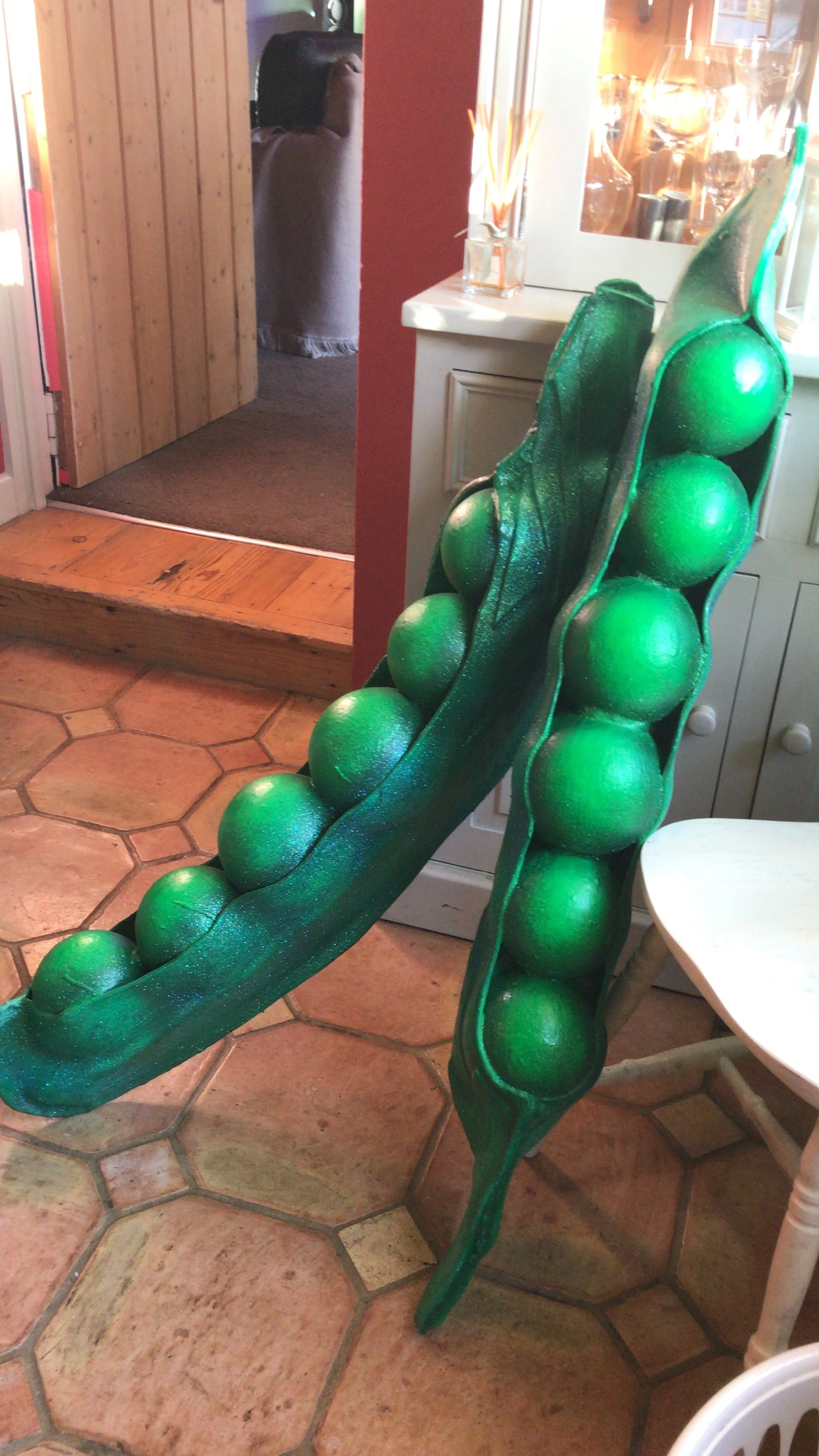 Decorative art piece resembling a pea pod with large green peas, displayed on a chair in a cozy indoor setting.