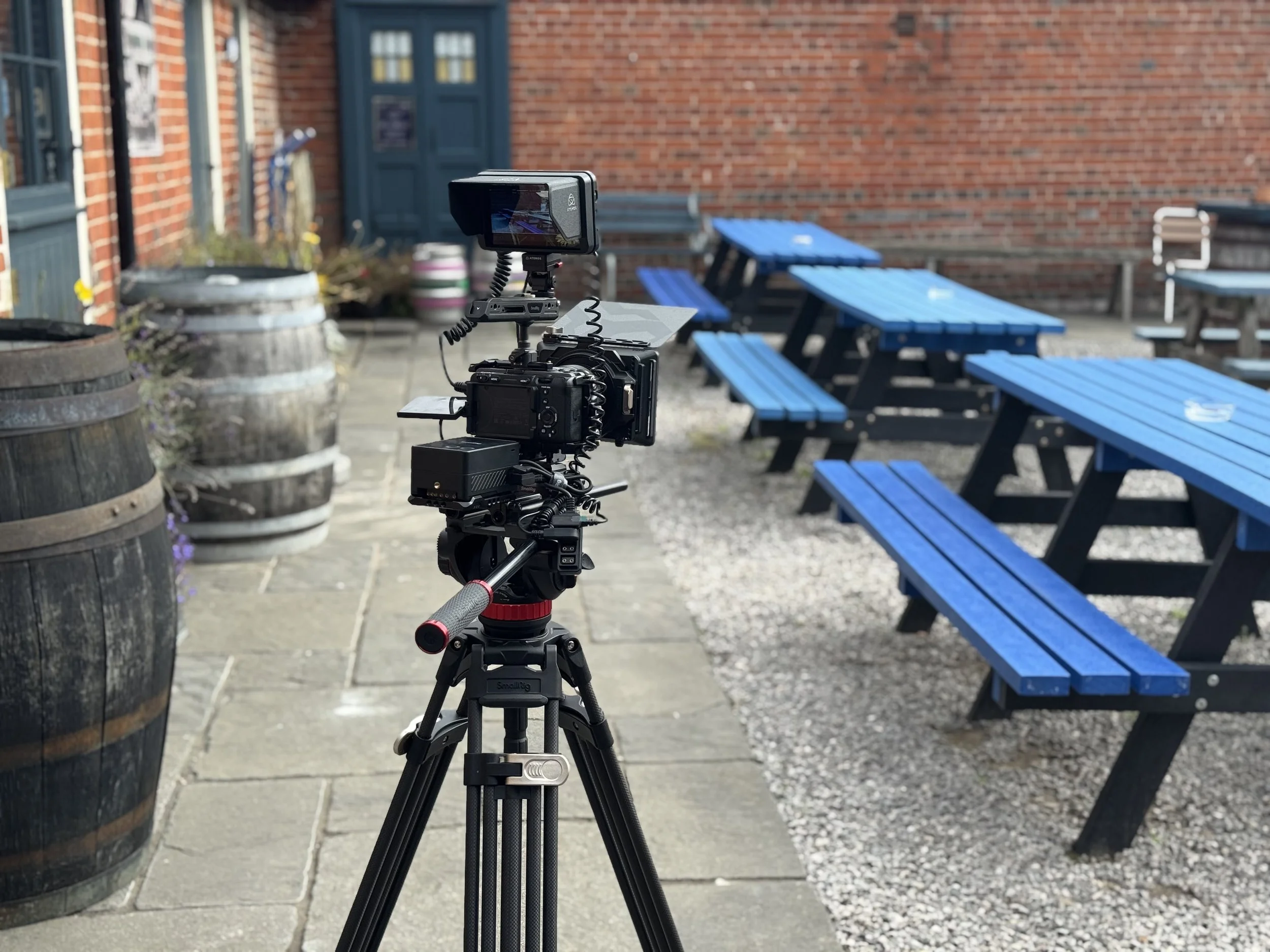 Camera setup on a tripod with blue picnic tables in the background at an outdoor patio with brick walls.