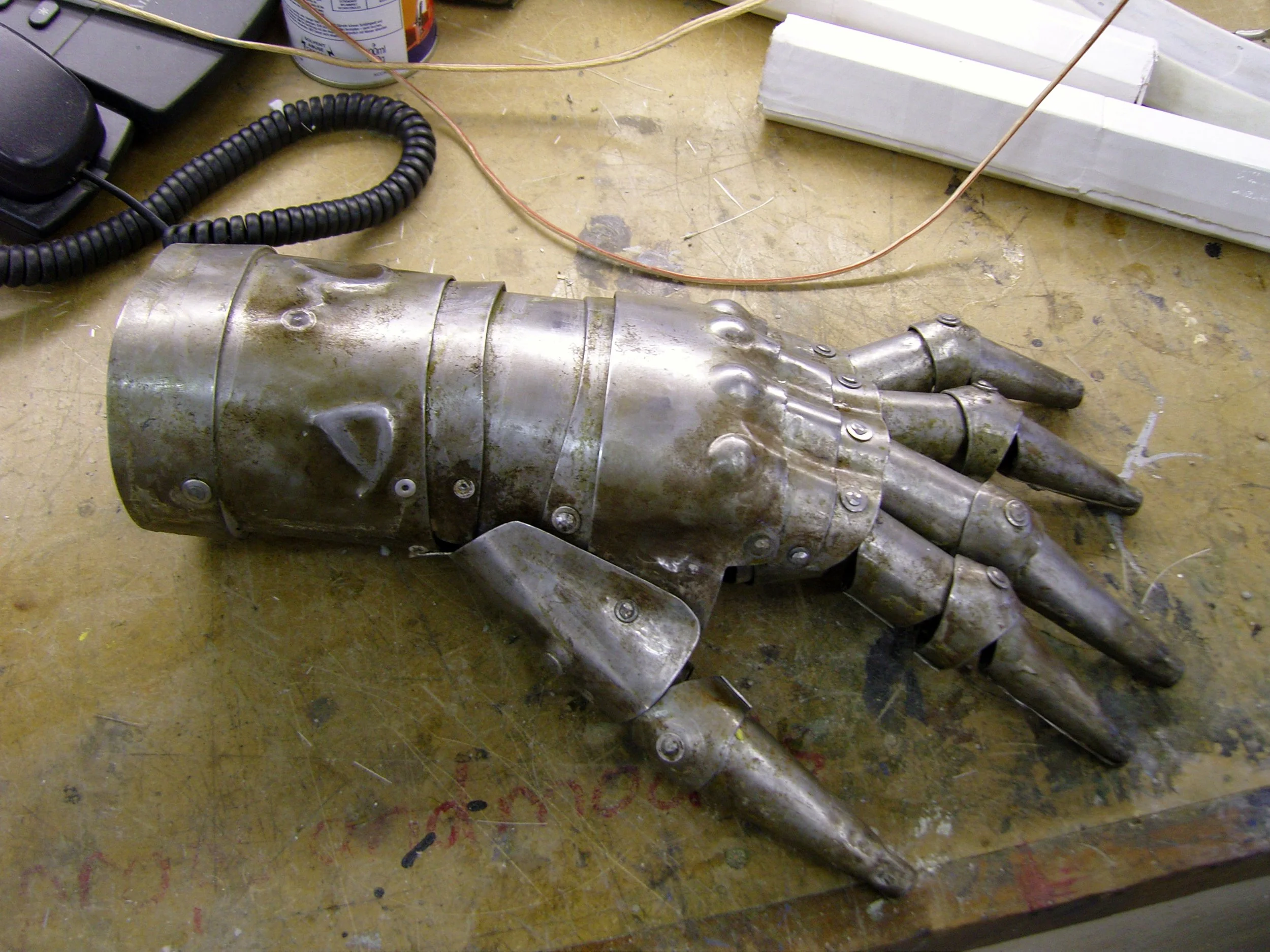 A metallic prosthetic hand or arm lying flat on a workbench, with visible joints and mechanical components.